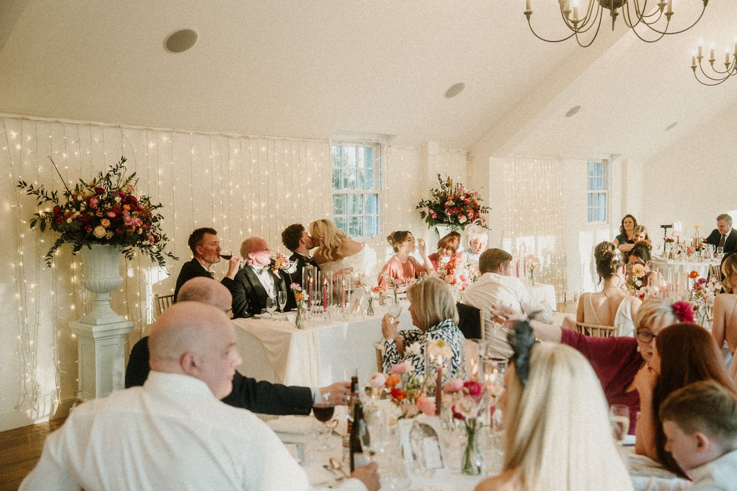Wedding guests enjoying a celebration in a bright, airy venue with twinkling lights.