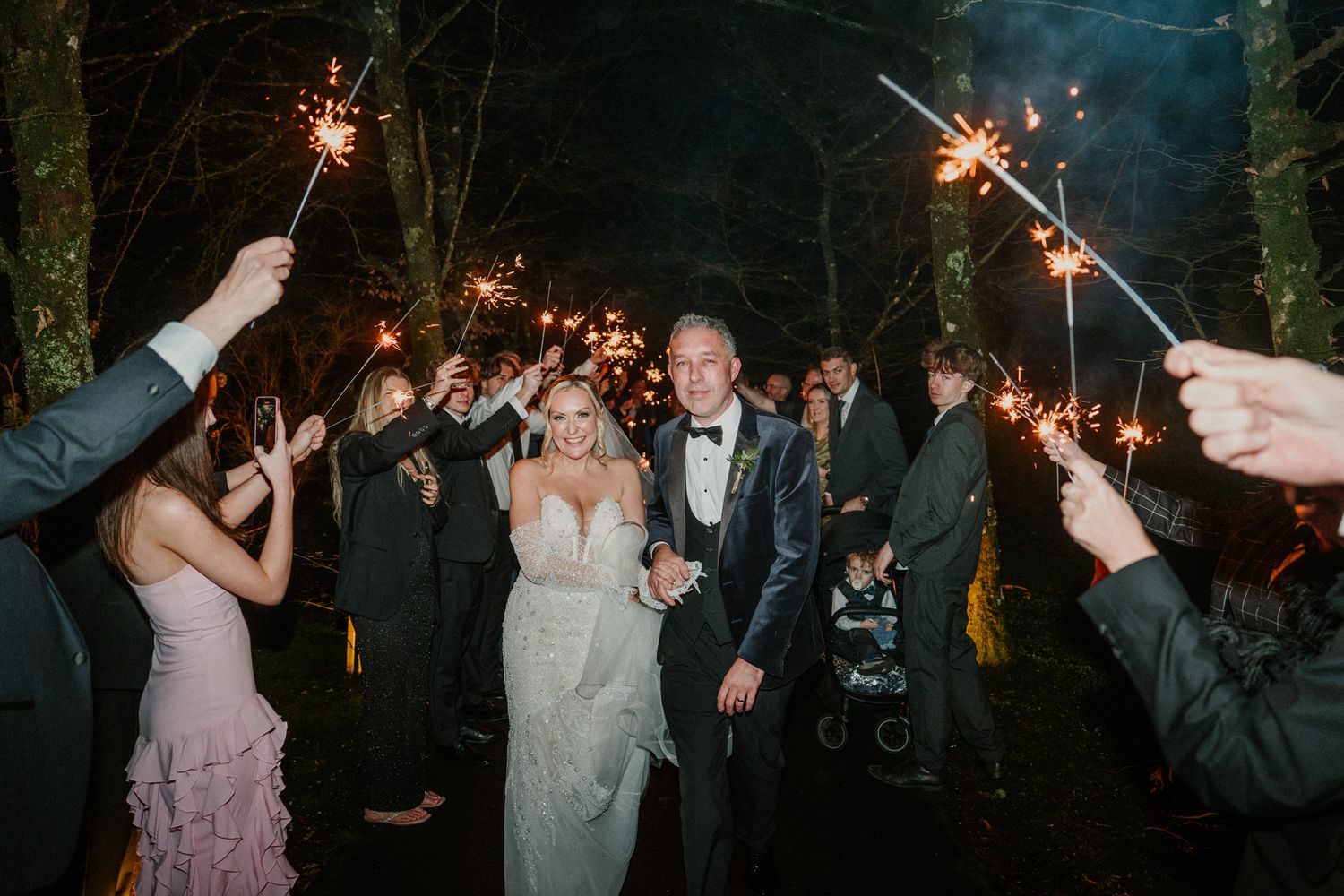 Guests wave sparklers creating trails of light during nighttime wedding festivities.