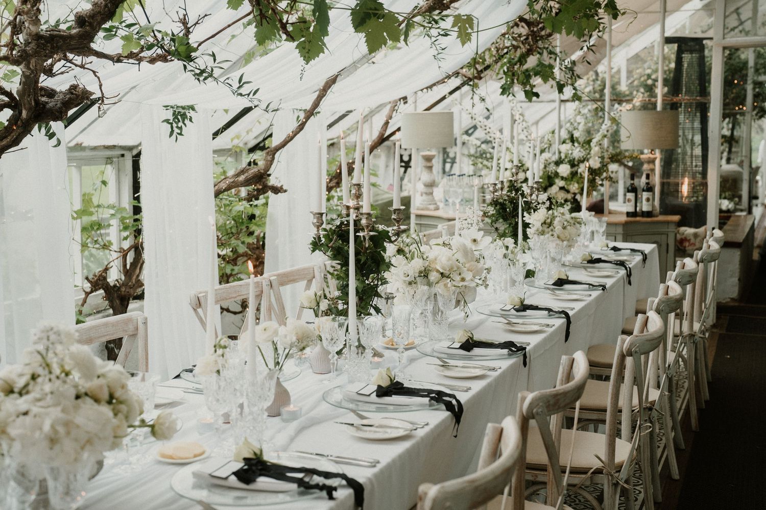 Elegant wedding reception tables decorated with white floral centerpieces and crystal glassware in a luxurious venue.