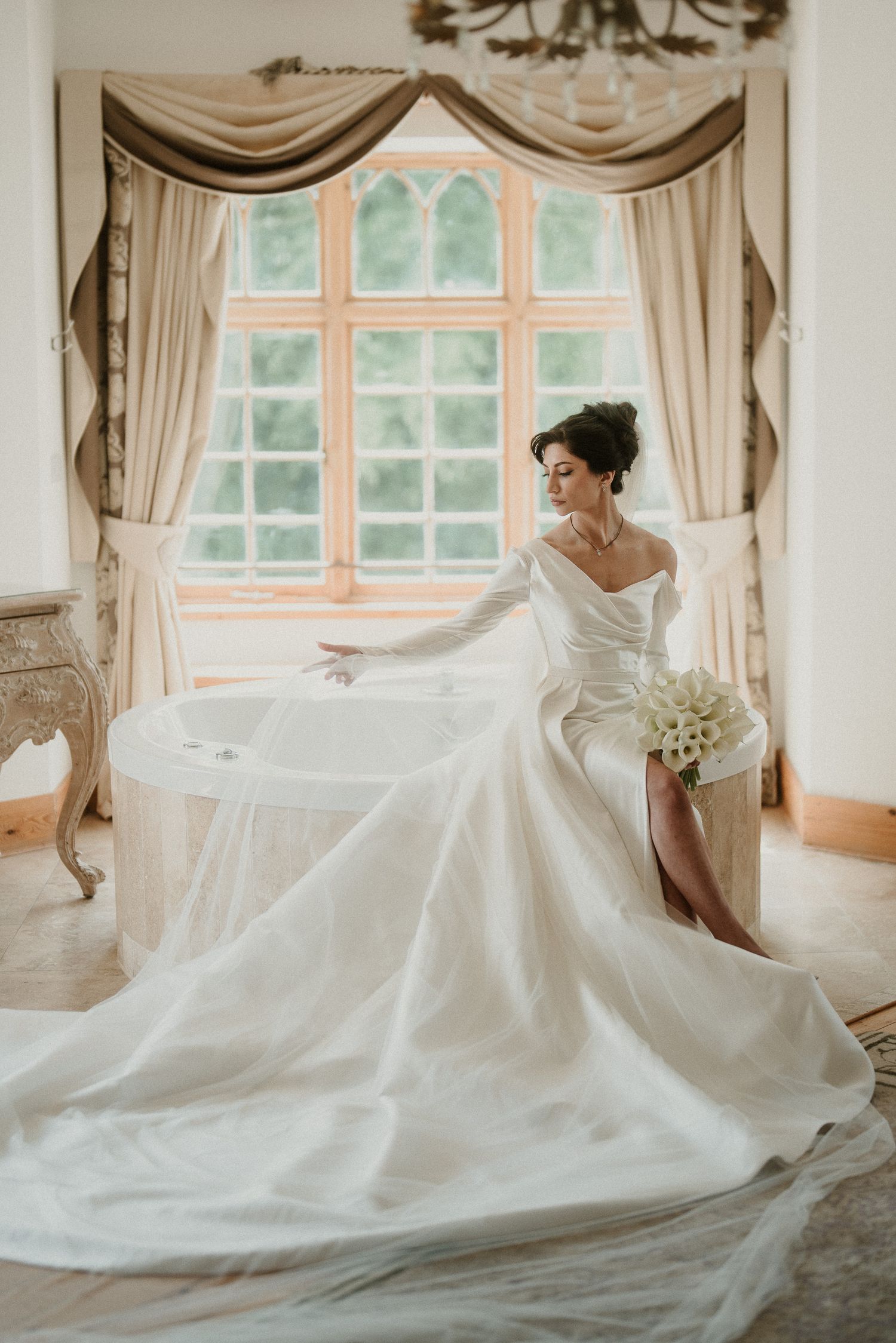 Elegant bridal portrait by a window with flowing white dress and bouquet.