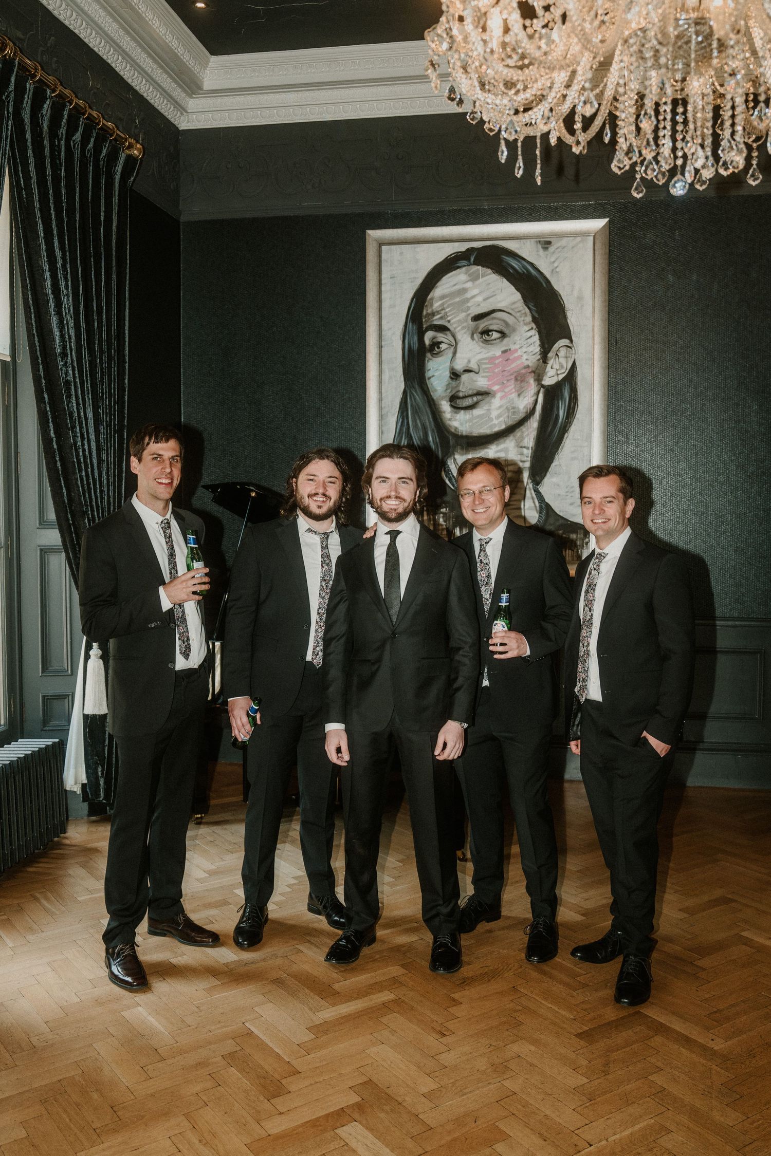 Group wearing formal attire posing in an elegant room with crystal chandeliers.