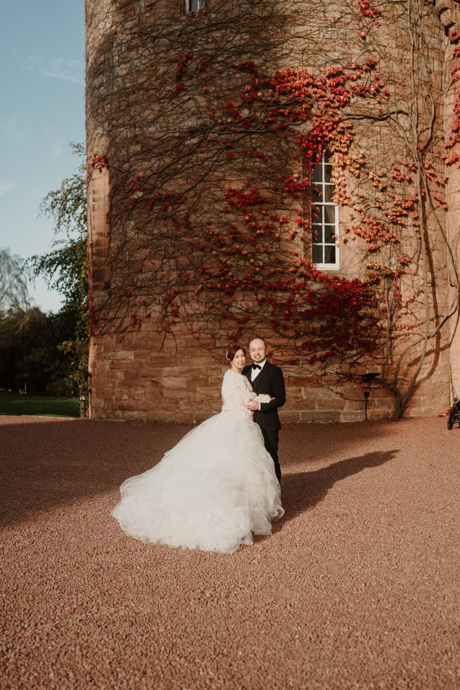A couple dances near a historic stone building covered in red autumn vines.