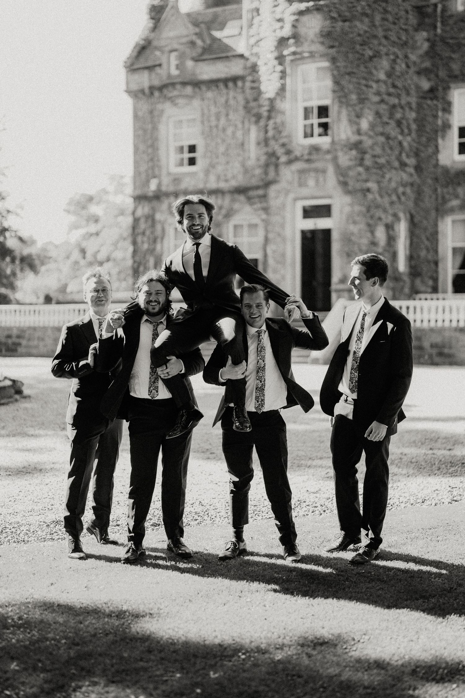 Black and white photo of groomsmen striking playful poses outside historic building.