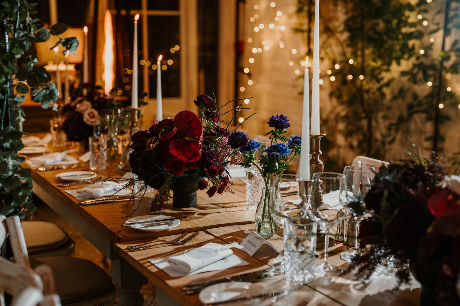 Cozy winter wedding table with deep red florals, tall white candles, and warm ambient lighting.