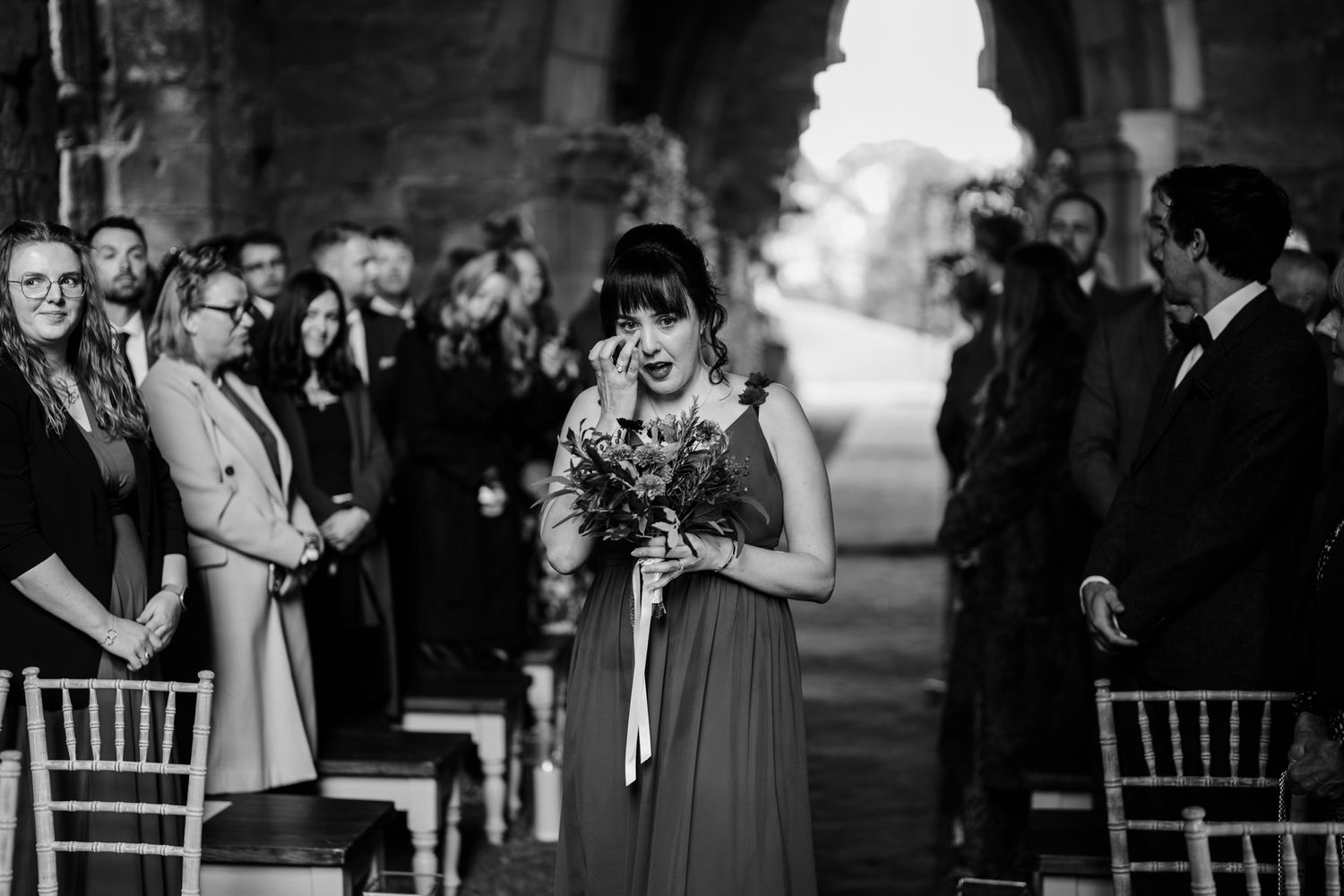 Monochrome image shows wedding ceremony gathering in gothic church architecture.