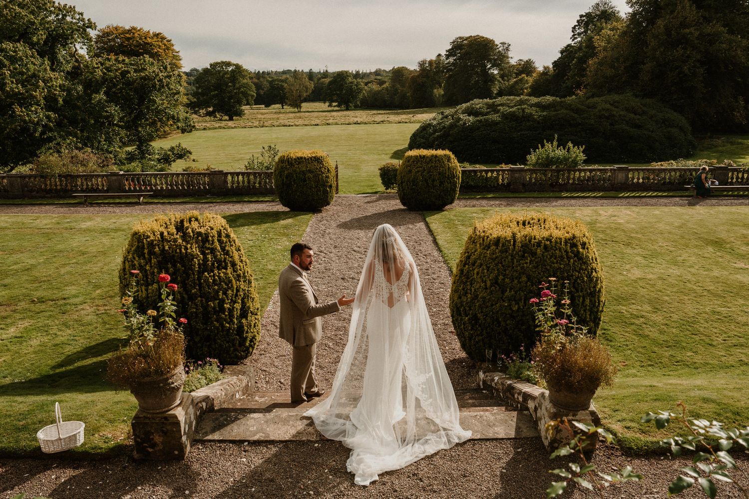 Bride and groom hold hands in a stunning English countryside garden, with manicured hedges and sweeping lawns.