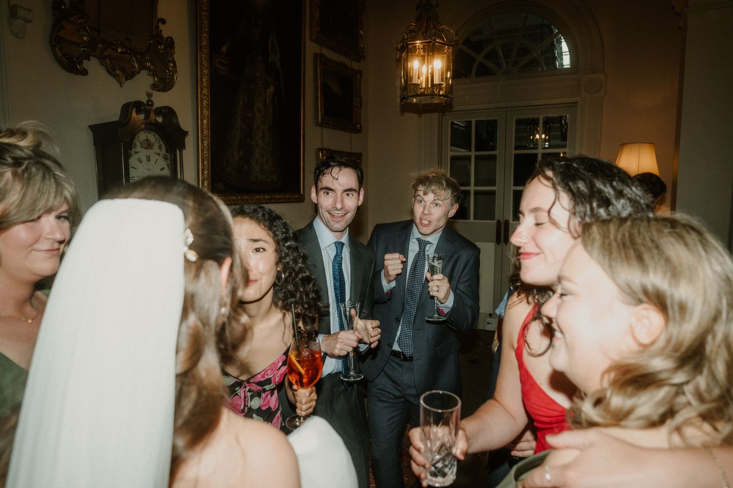Wedding guests smiling and toasting with champagne glasses at an elegant indoor reception venue.