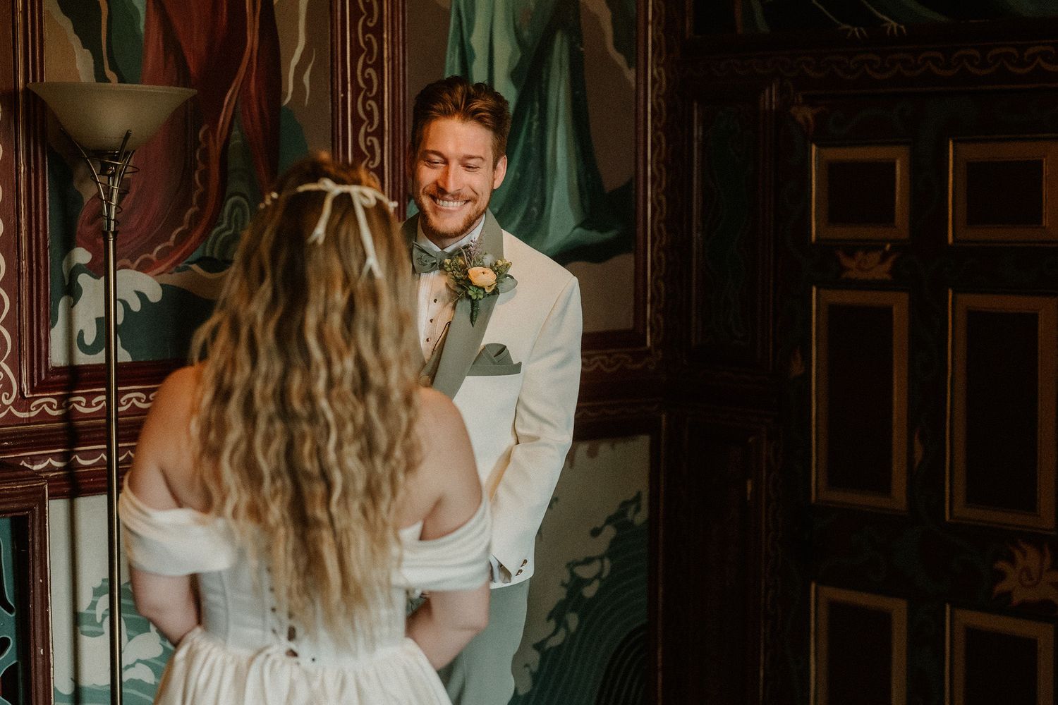 Groom smiling at bride during first look moment at elegant wedding venue with ornate decor.