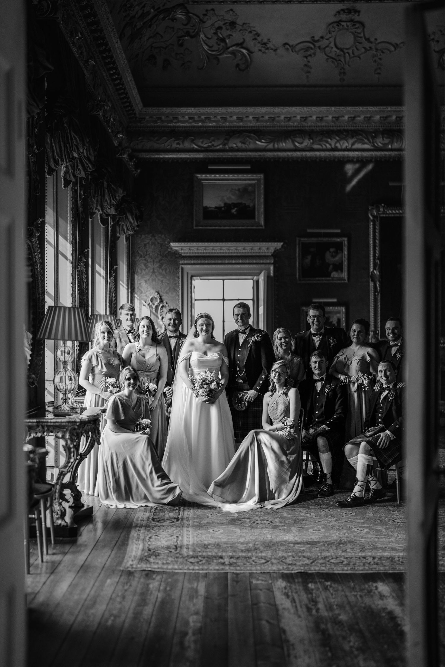 Dramatic black and white panorama of wedding party in grand historic hall.