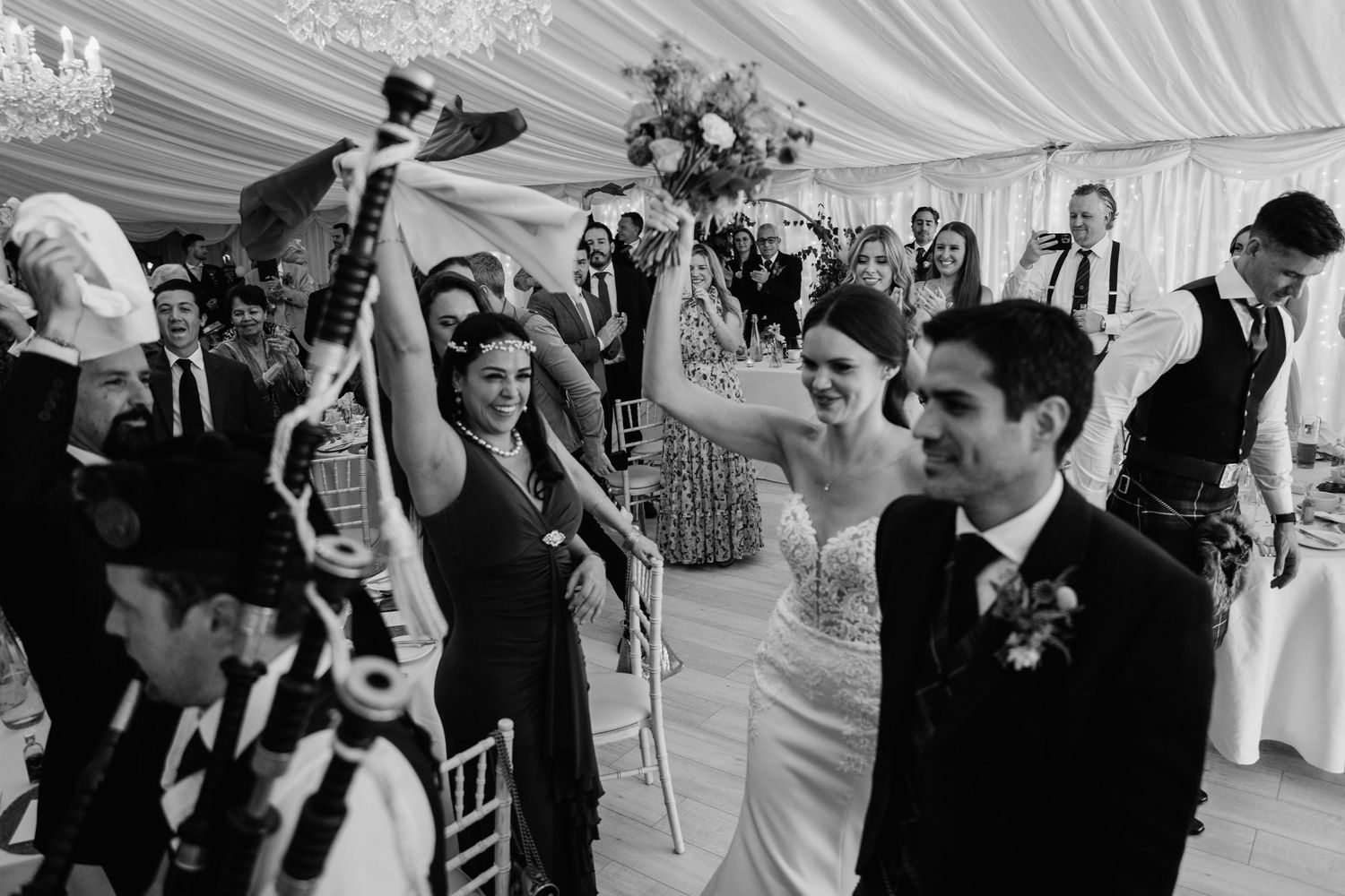 Energetic dancing and celebration at Scottish wedding reception under draped tent ceiling.