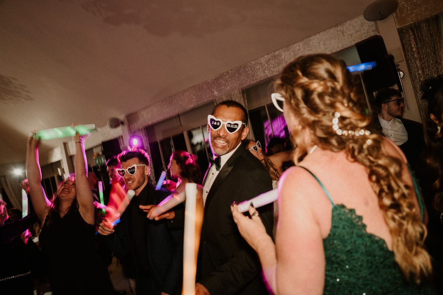 Wedding reception dance floor with colorful lighting and guests wearing party accessories.