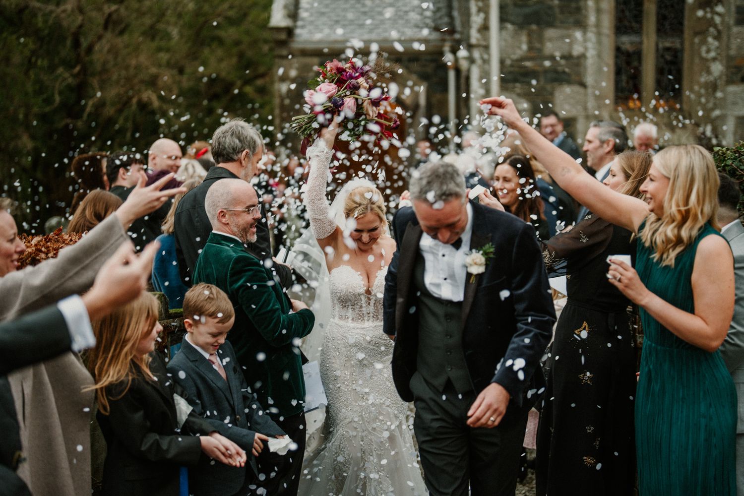 Wedding guests shower the newlyweds with confetti during an outdoor celebration.