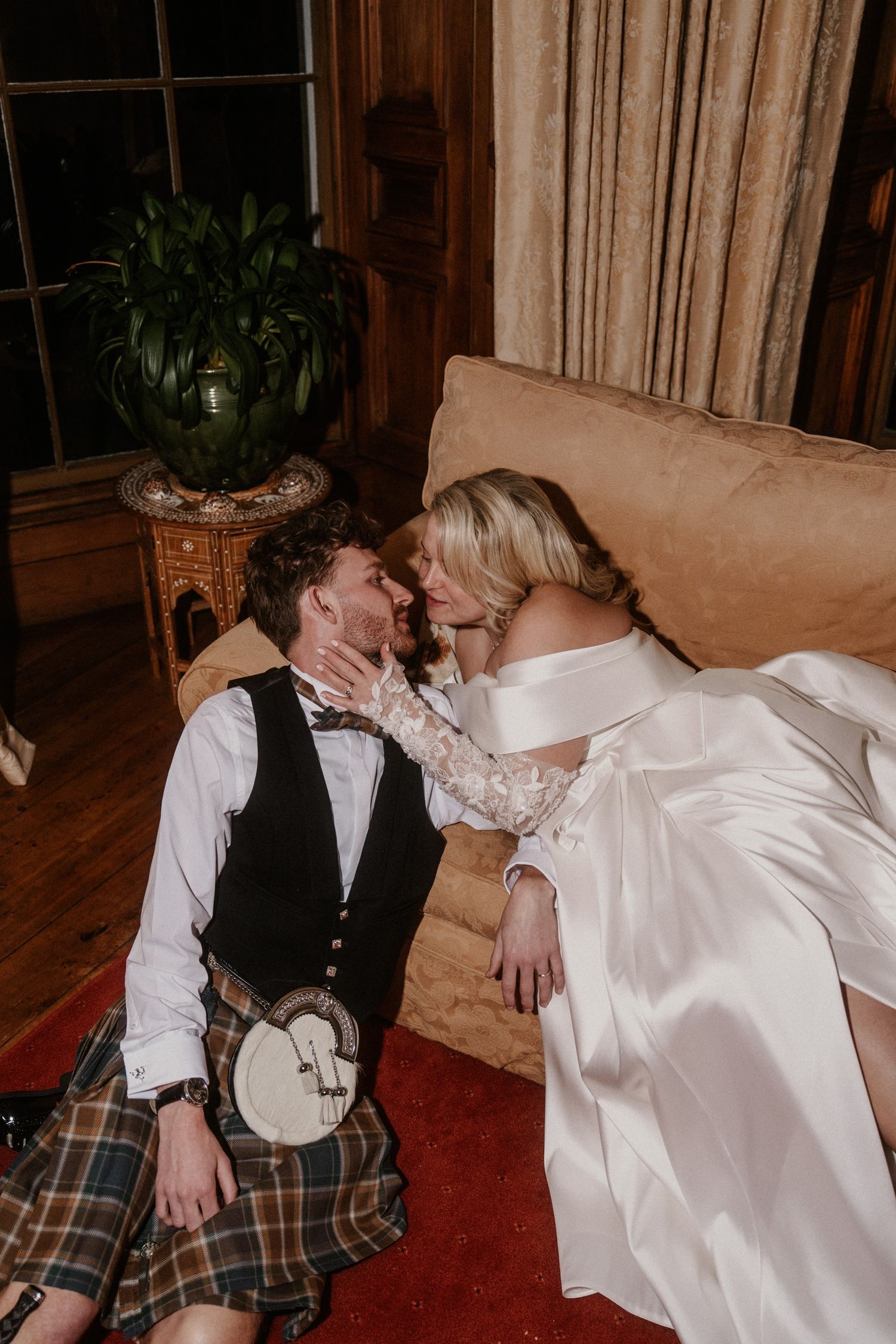 Wedding couple sharing romantic moments on a couch in a warmly lit room.