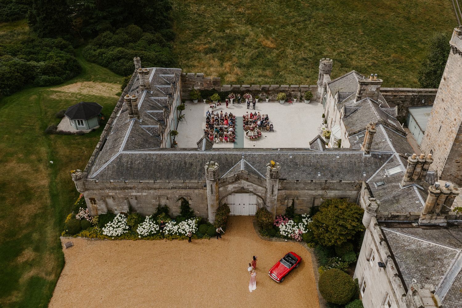 Aerial view of historic stone castle venue with manicured gardens and wedding setup.