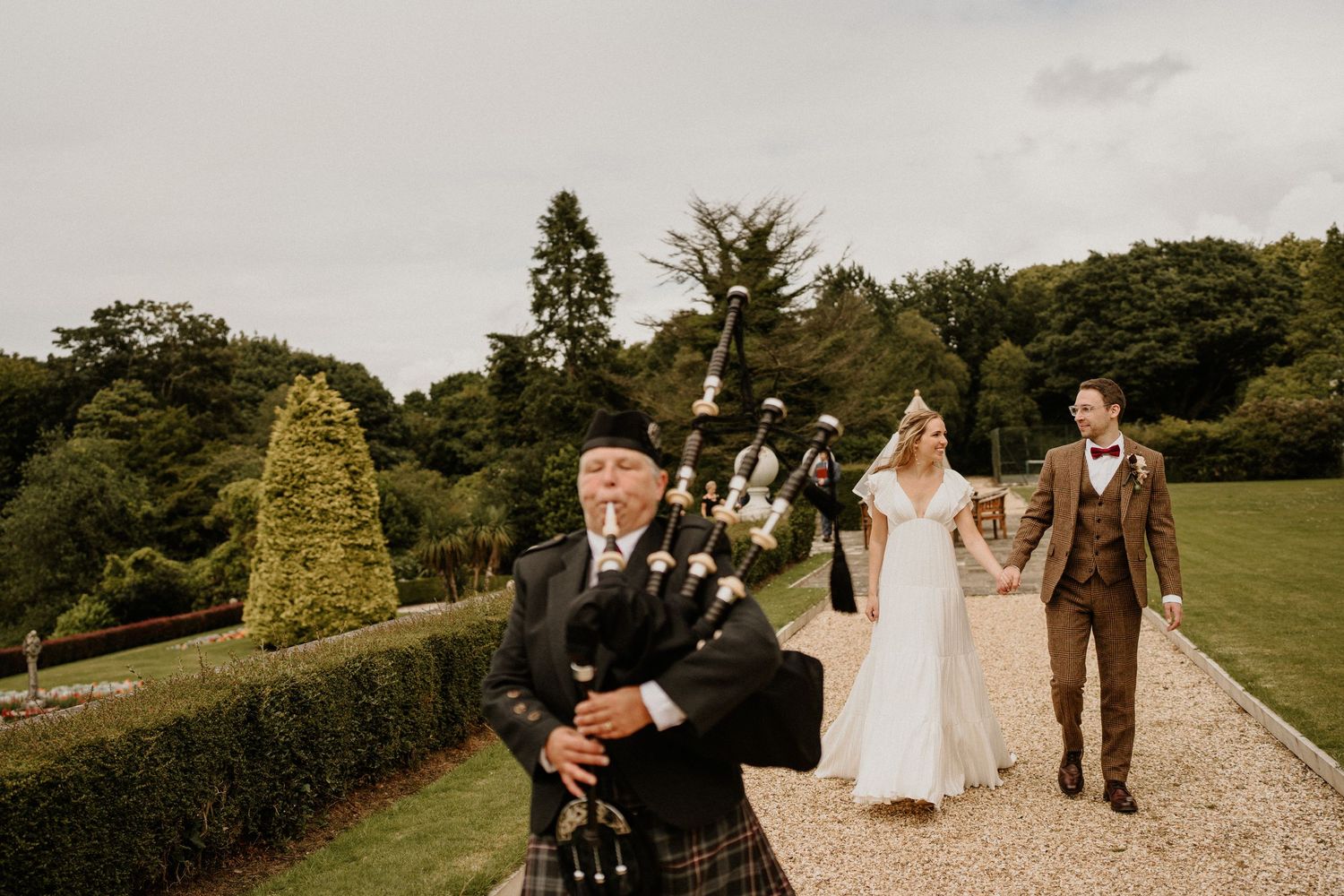 A bagpiper leads a wedding procession along a garden path at a Scottish estate.