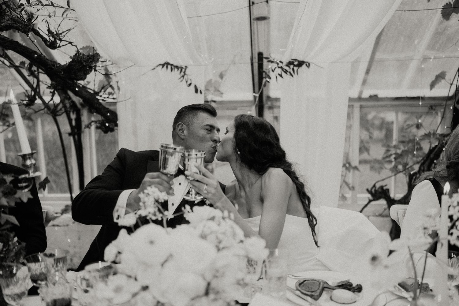 Black and white photo of newlyweds sharing an intimate moment at their reception table.