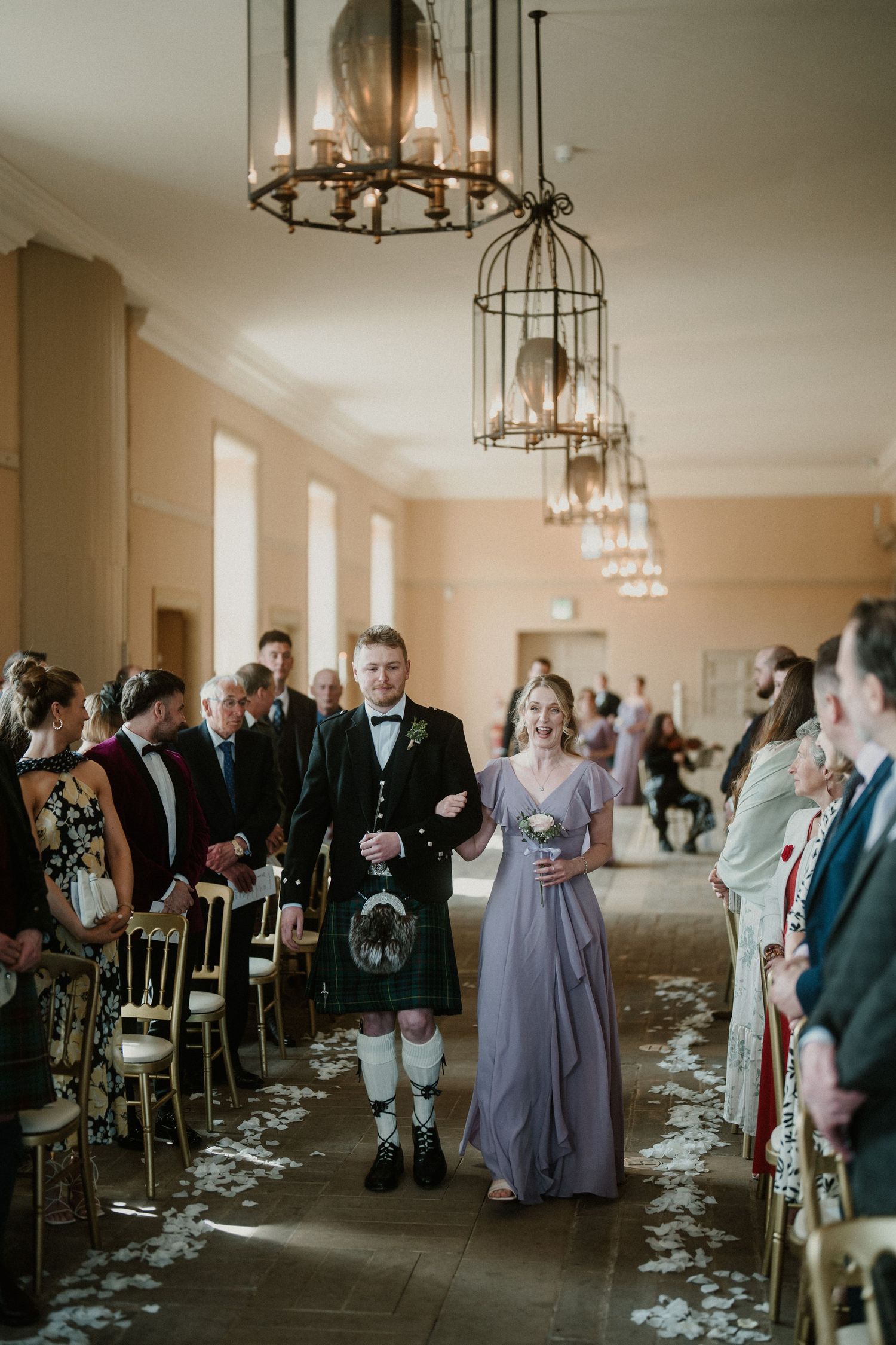 Wedding reception hall with hanging chandeliers and scattered petals along the aisle.