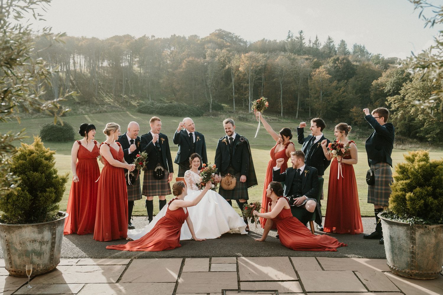 Large wedding party in red dresses and formal attire gathered on stone terrace.