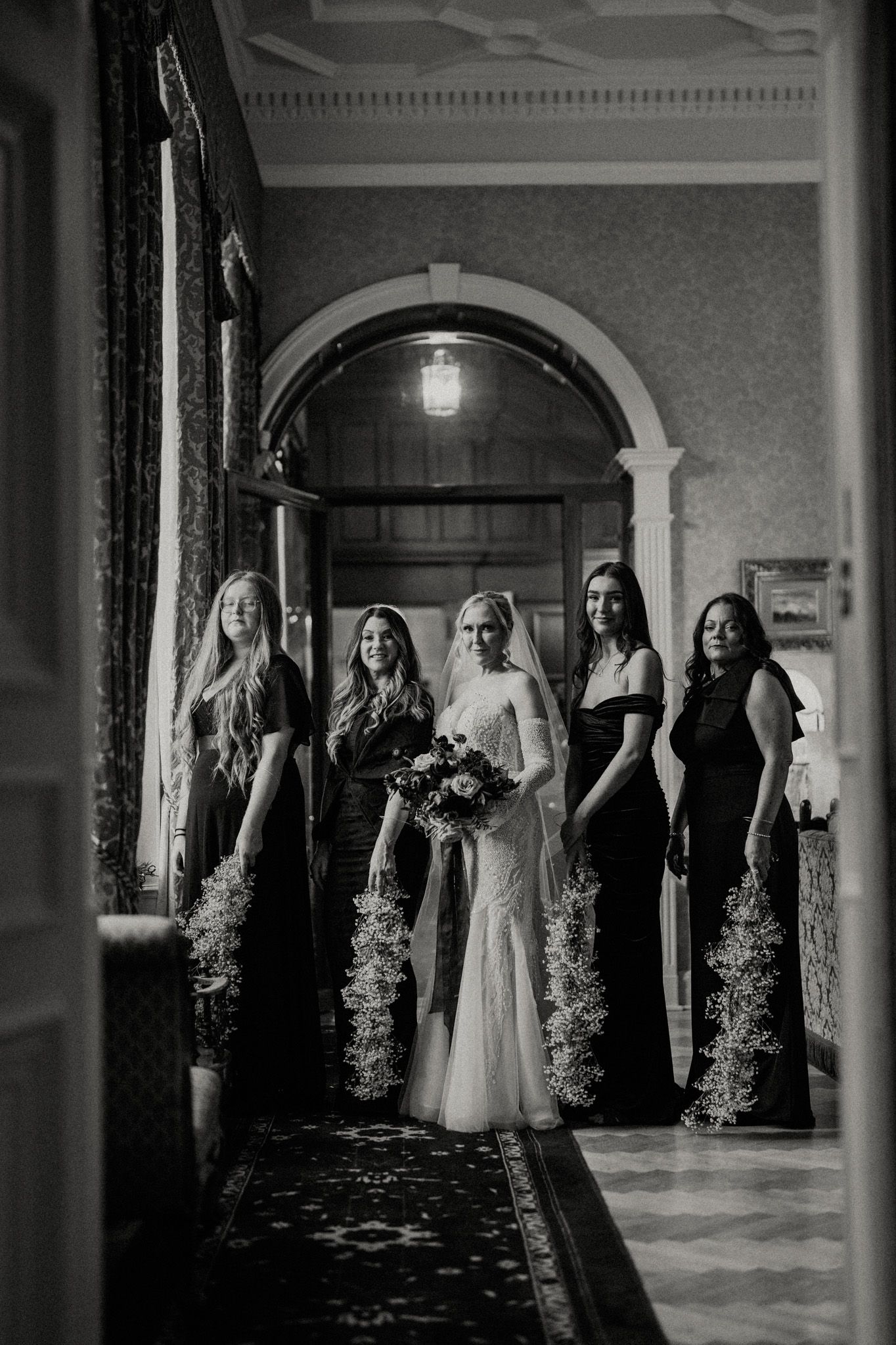 Dramatic black and white wedding party photo in an elegant hallway with architectural details.