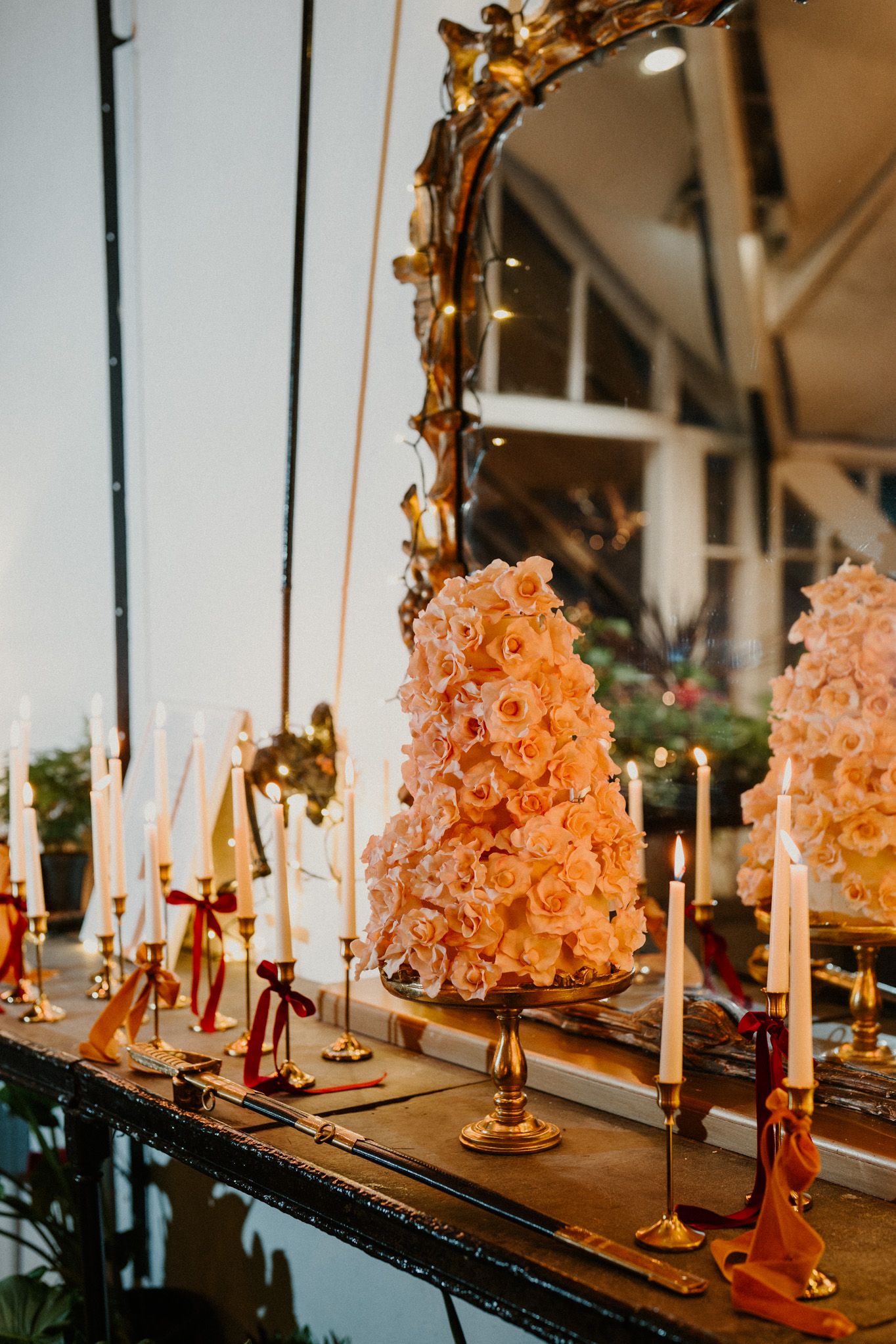 Ornate table display featuring peach-colored floral arrangements and golden candelabras against a mirrored surface.