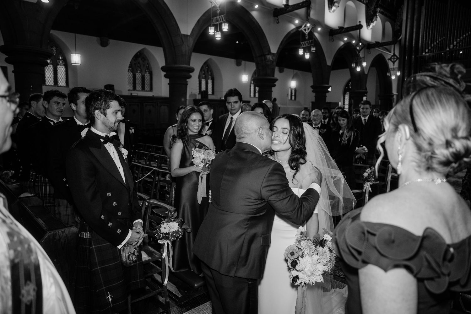 Black and white photo of wedding celebration inside ornate church with arched architecture.