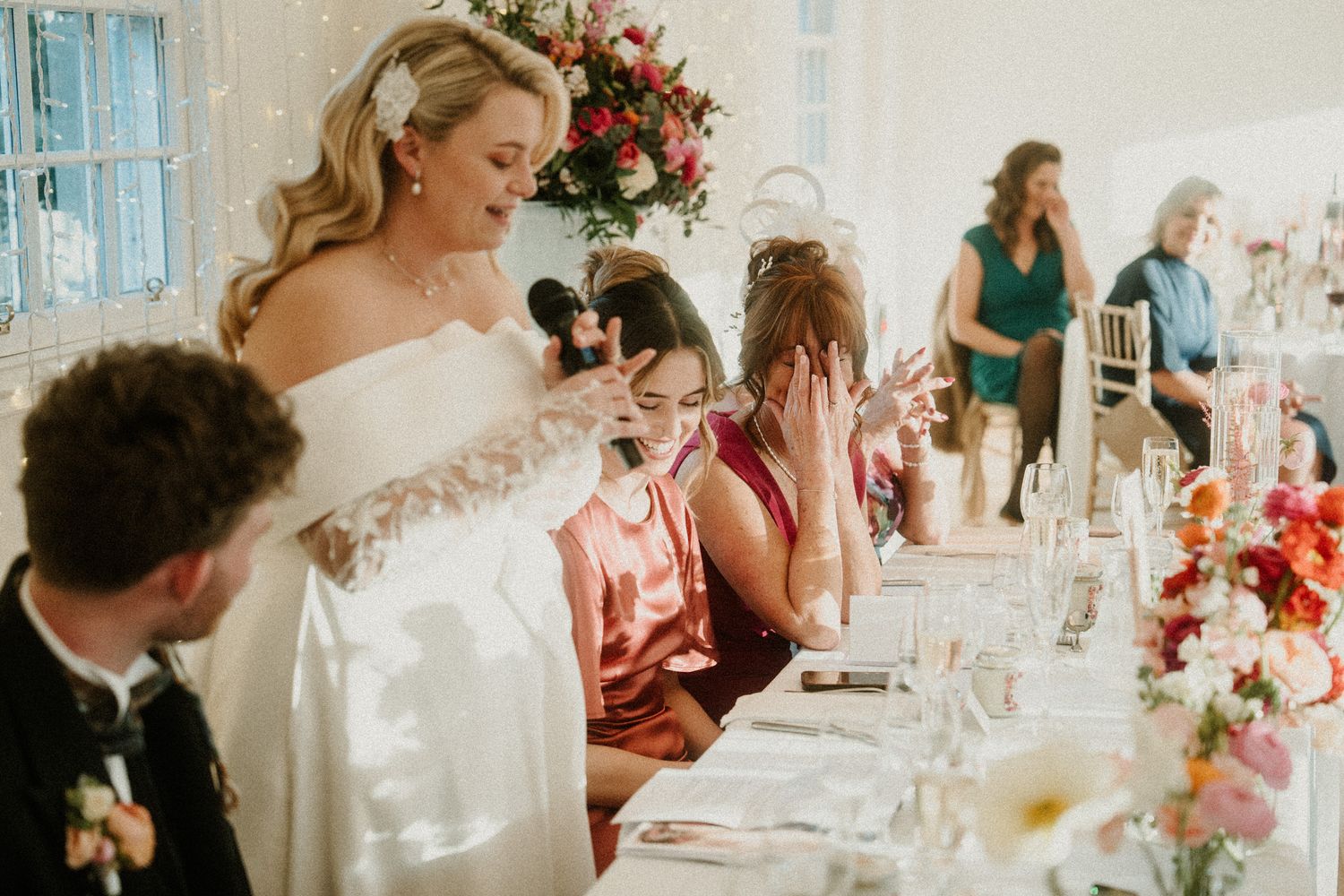 Elegant wedding reception in a bright white room with twinkle lights and floral centerpieces.