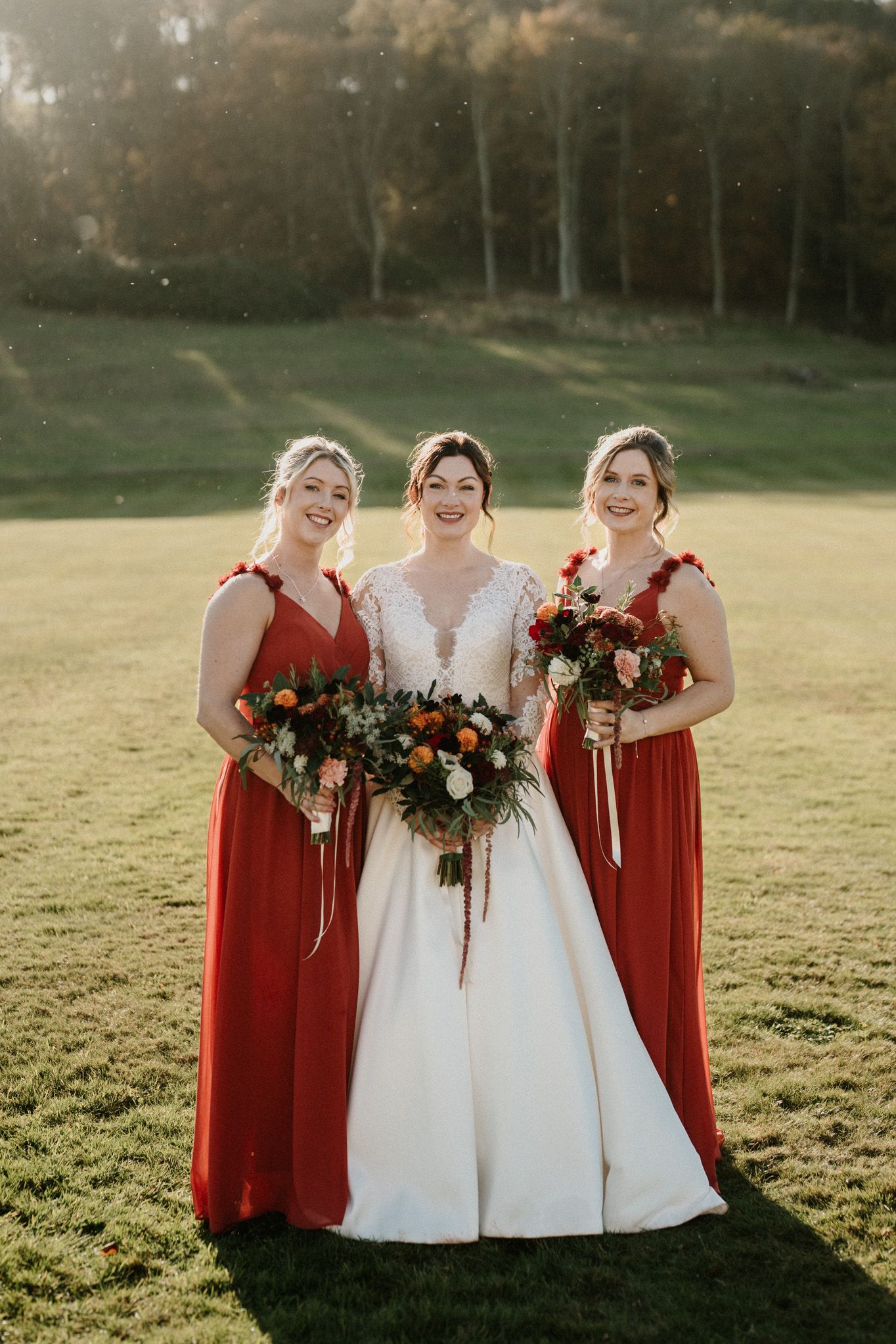 Three women in wedding attire share laughter during golden hour outdoor portrait.