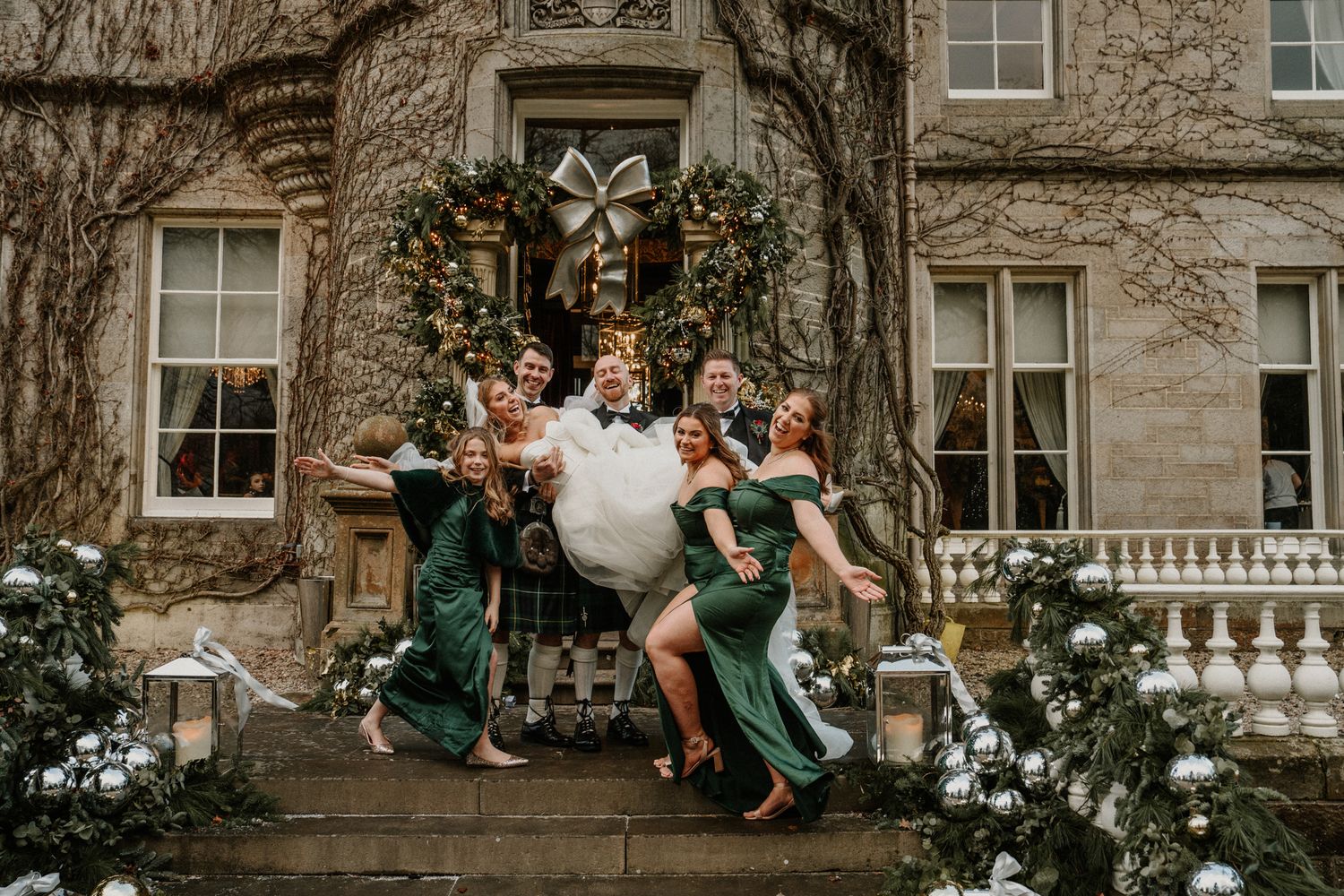 Bridesmaids in emerald dresses pose playfully on stone steps of castle.
