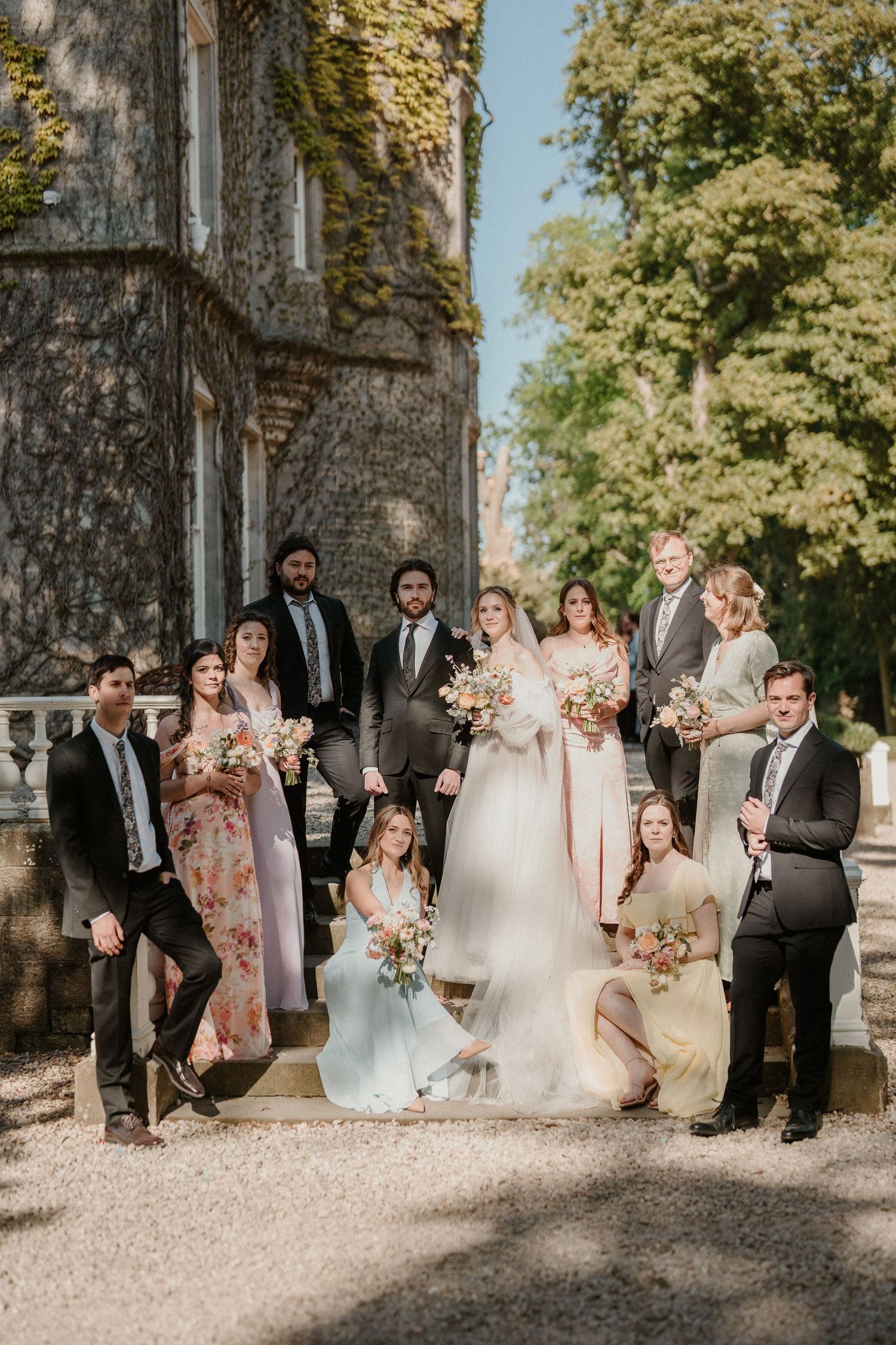 Wedding party poses together against stone castle wall in formal attire with pink floral accents.
