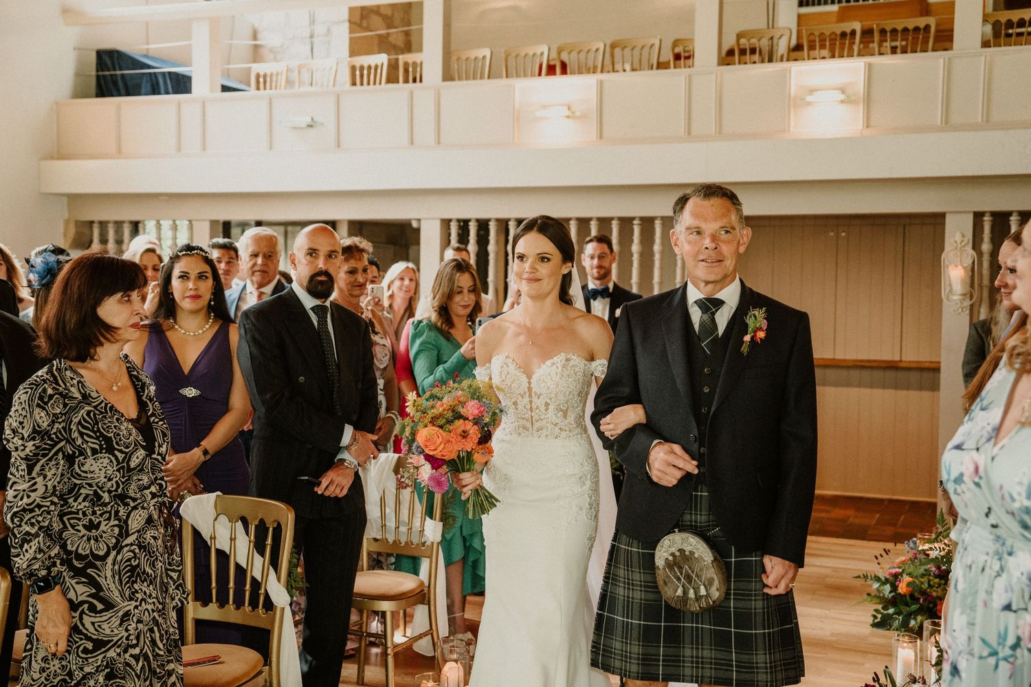 Wedding reception scene with guests celebrating in an indoor venue with warm lighting.