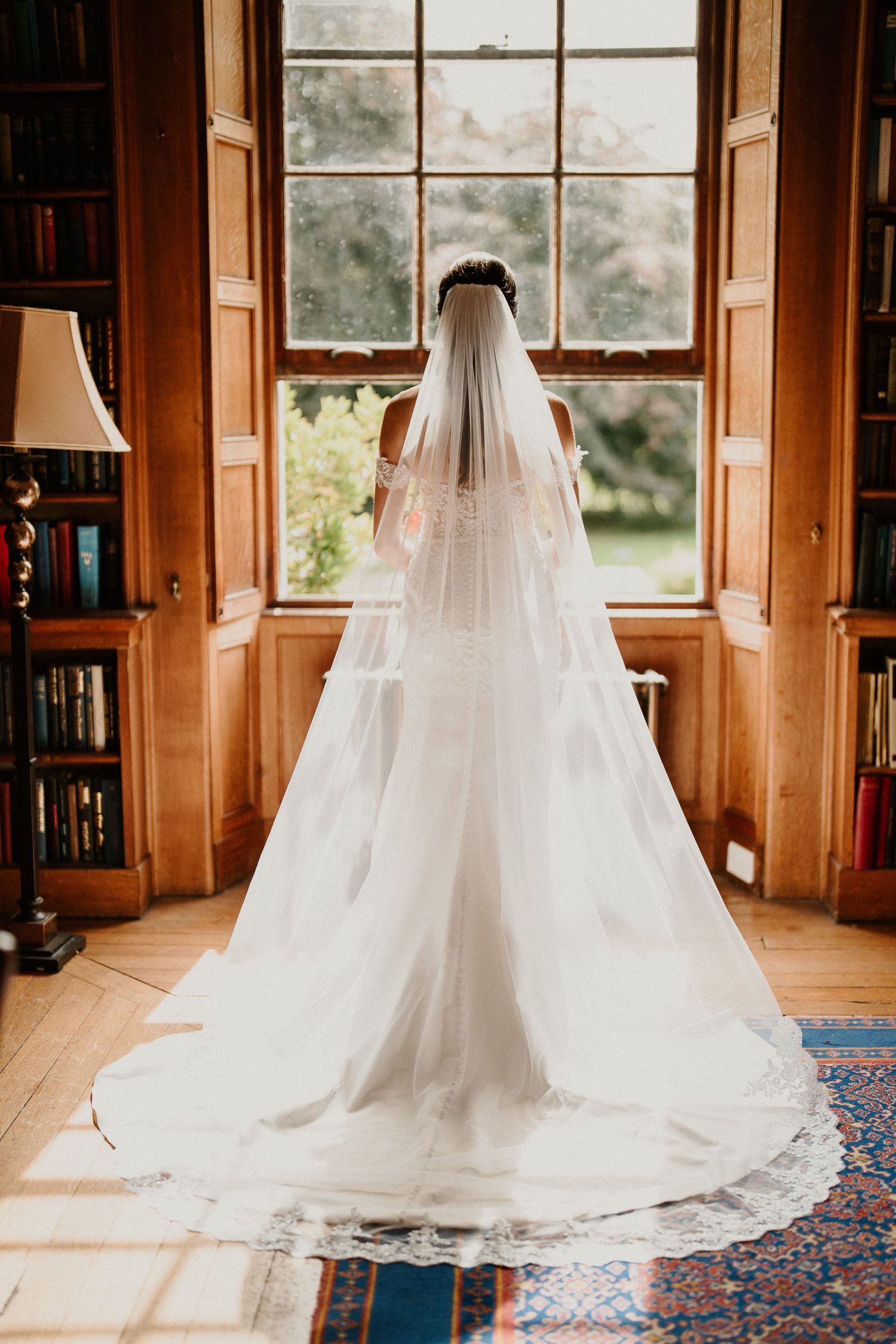 Sunlit wedding dress with cathedral veil photographed in a classic library interior.