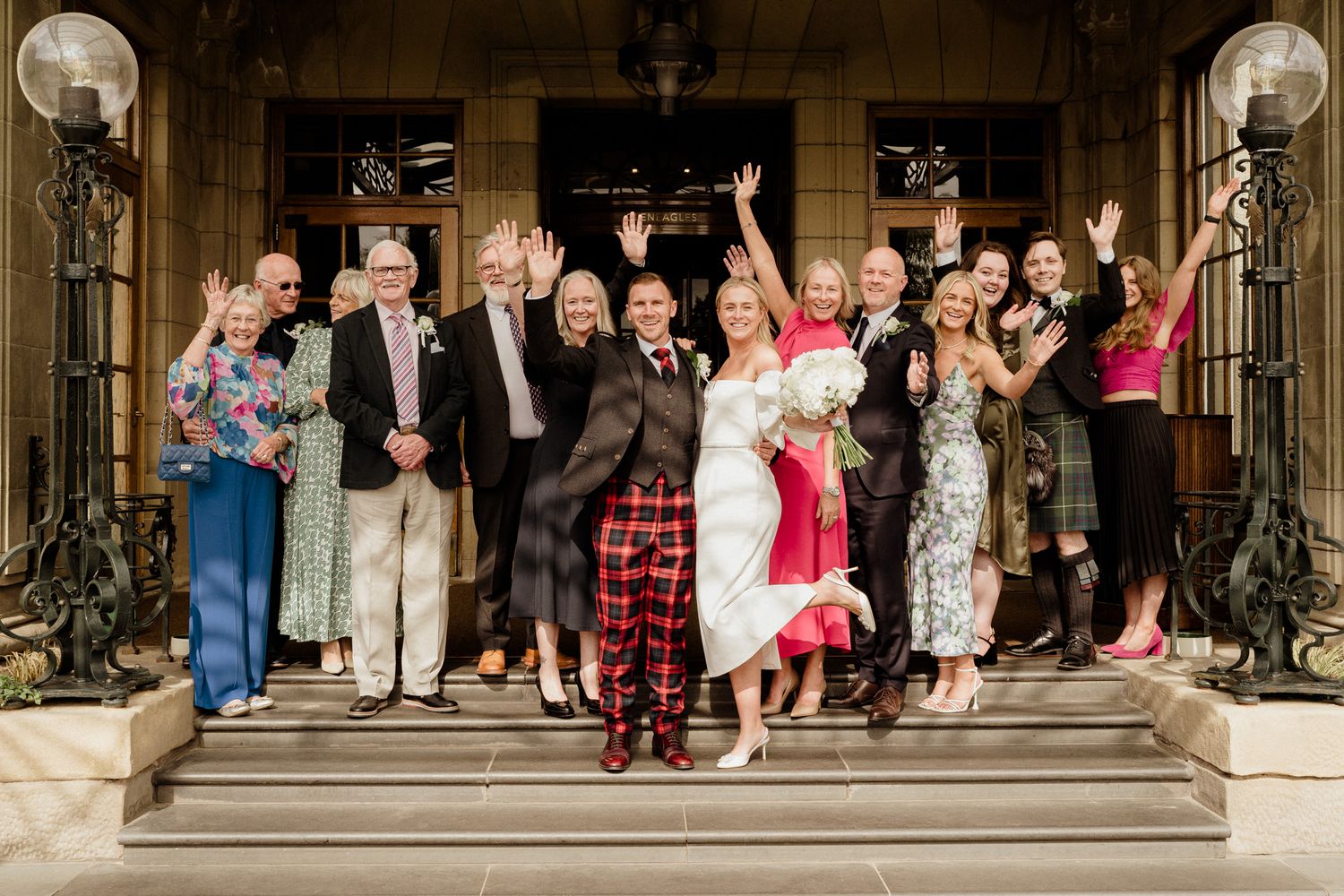 Wedding party and guests posed on grand exterior steps of a historic venue.
