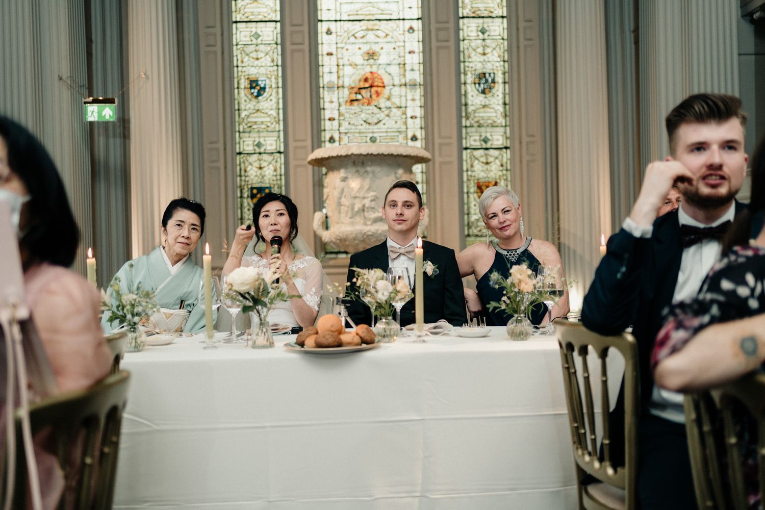 Wedding reception hall with stained glass windows and formal table settings.