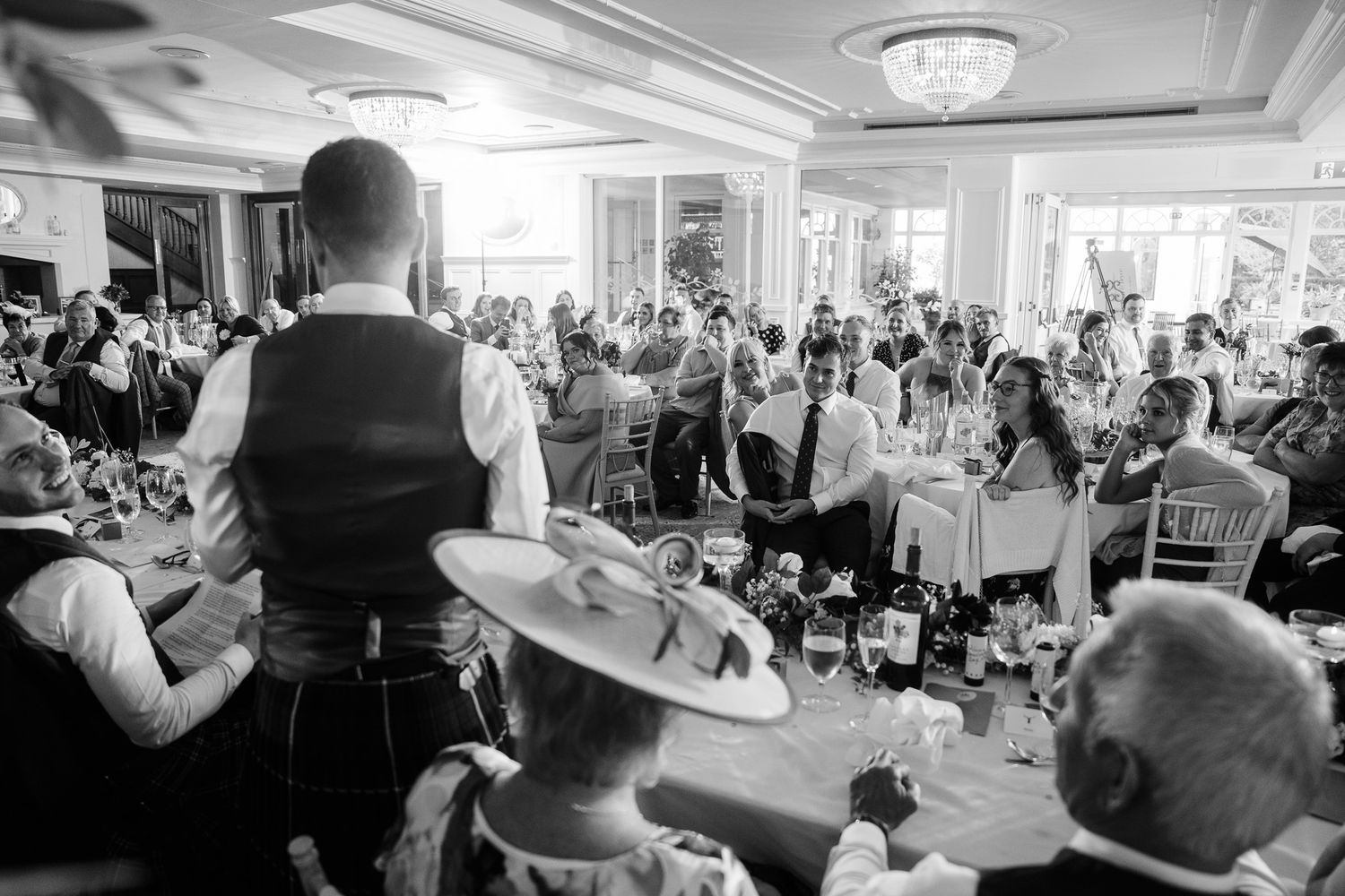Black and white photo of wedding guests celebrating in a bright banquet hall.