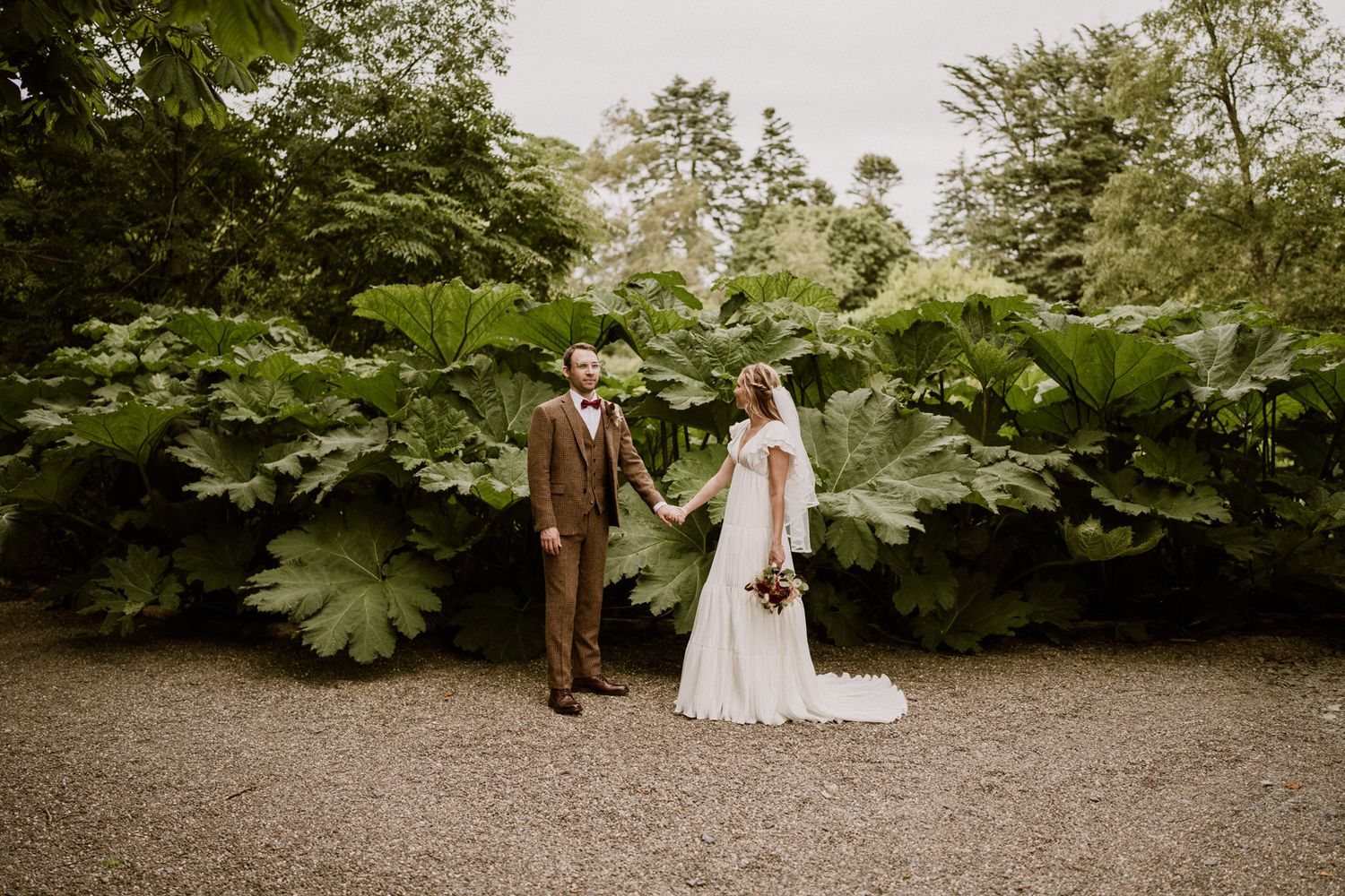 A couple shares an intimate moment on a garden path surrounded by verdant foliage.