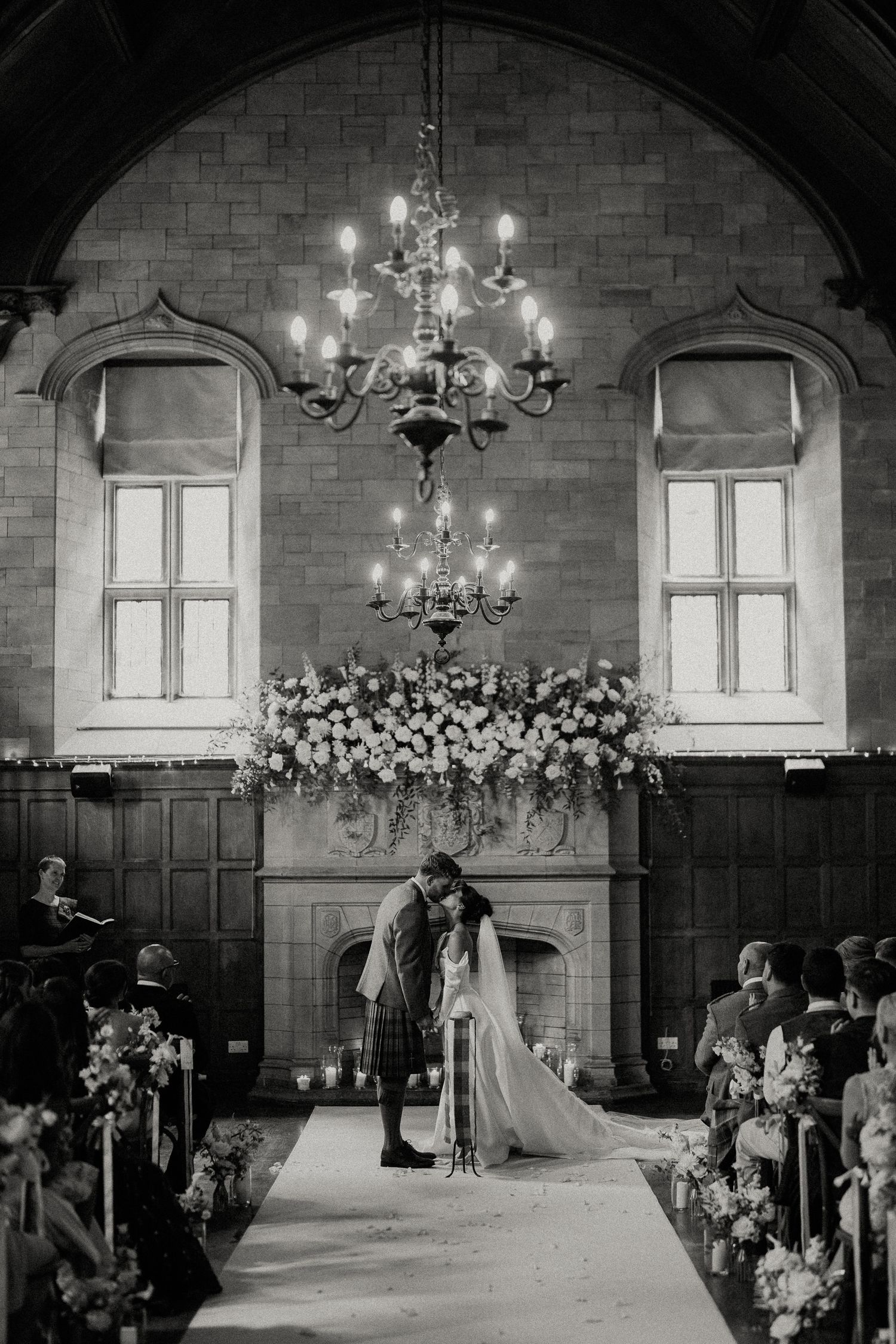 Wedding ceremony venue with stone walls, chandeliers, and floral arrangements decorating the altar area.