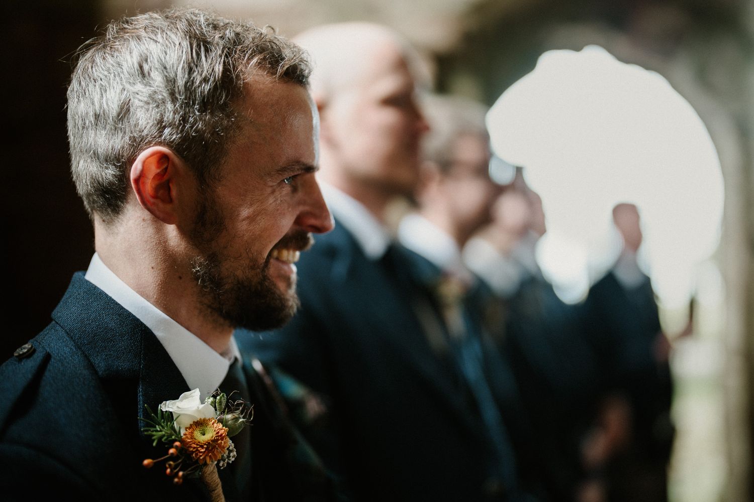 Wedding guests gathered in stone church with natural light streaming through arched windows.