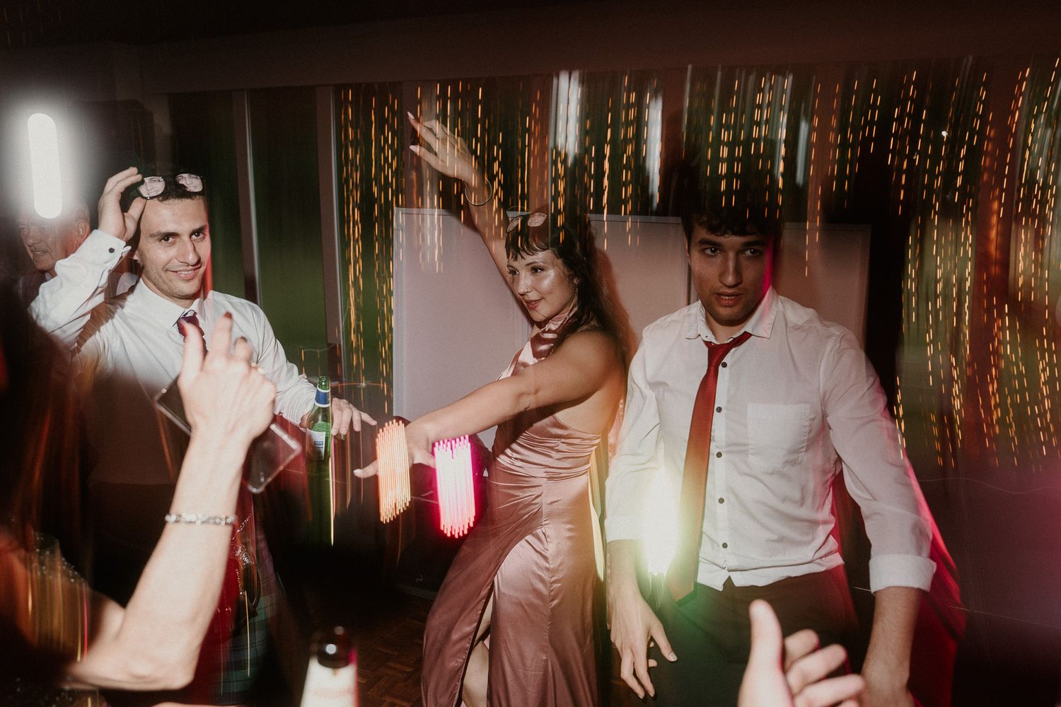 Party guests dancing energetically under colorful streamers and ambient lighting at a wedding reception.