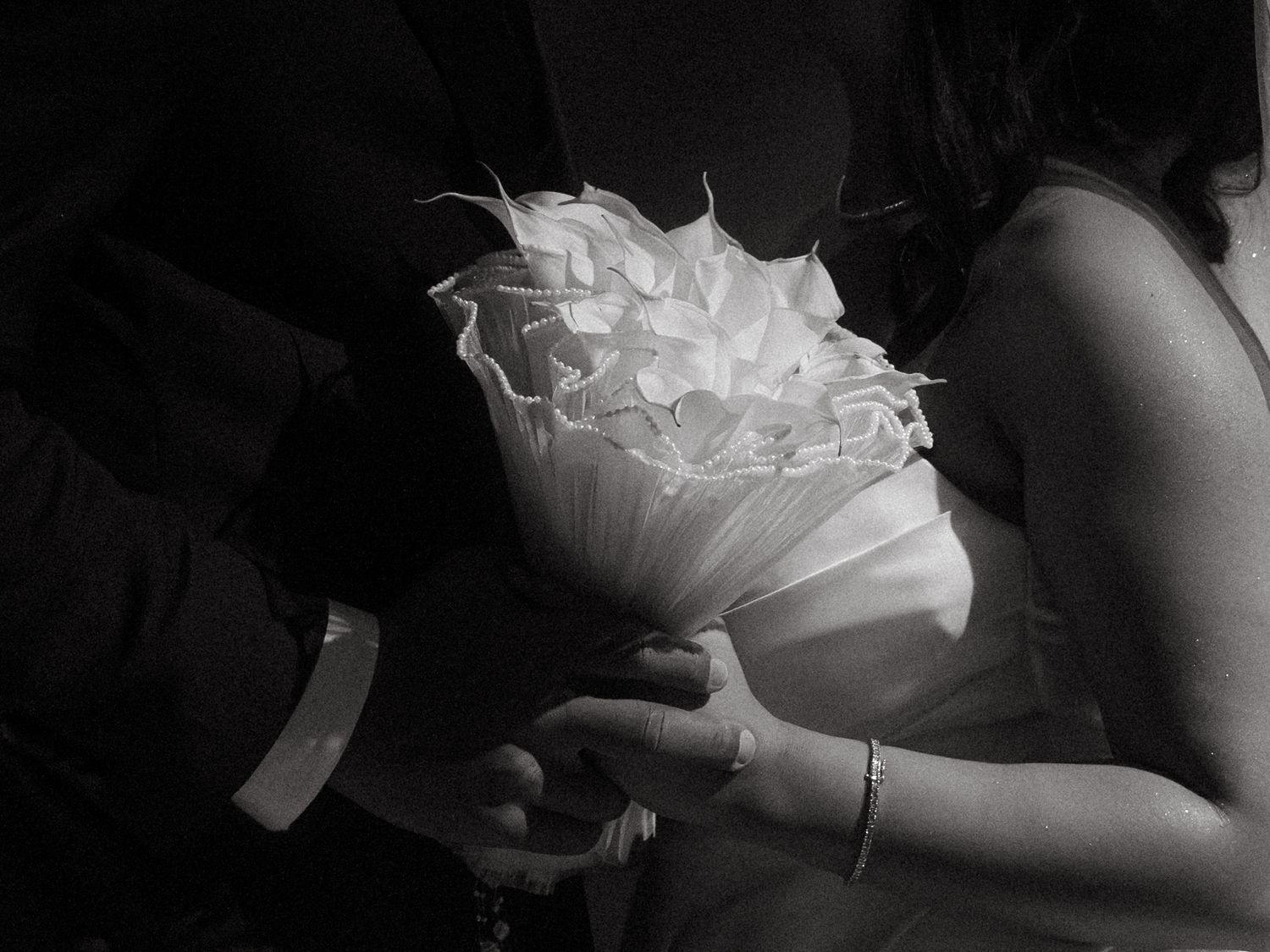 Black and white close-up of bride and groom holding an elegant white floral bouquet with layered petal details.