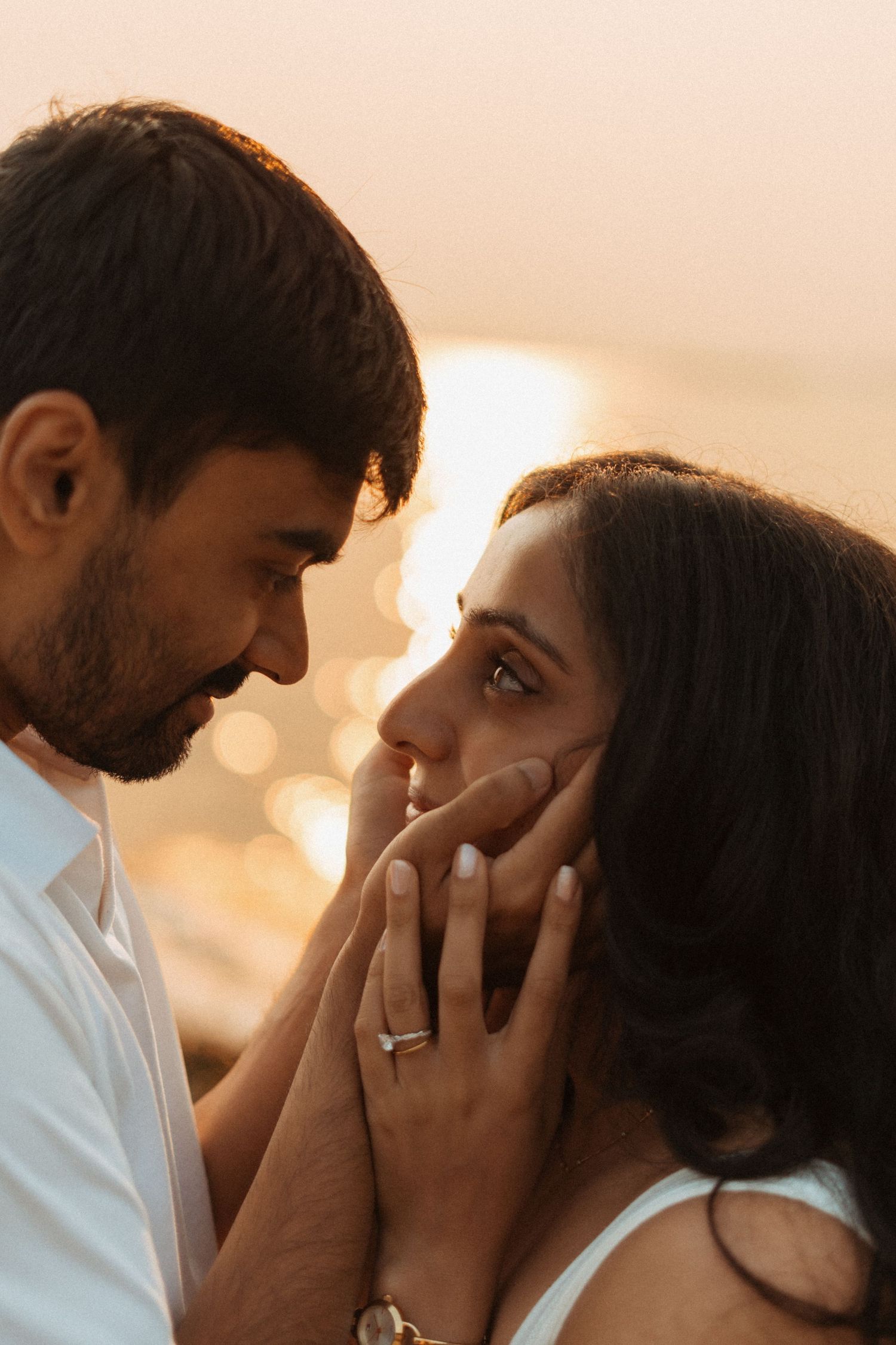 Romantic couple sharing an intimate moment at golden hour, woman wearing engagement ring, warm sunset bokeh background.