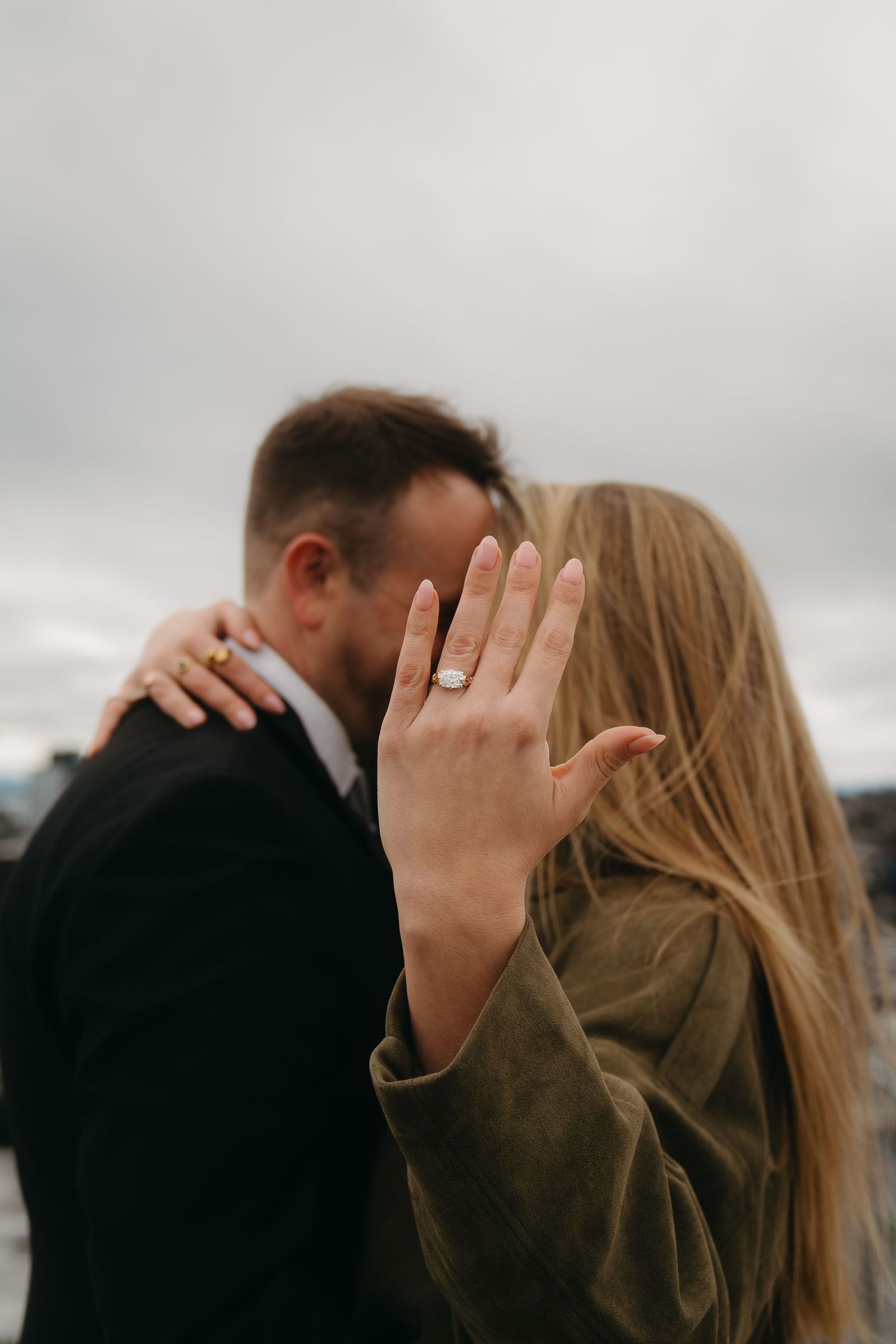 Newly engaged couple kissing while bride displays her diamond engagement ring to camera.