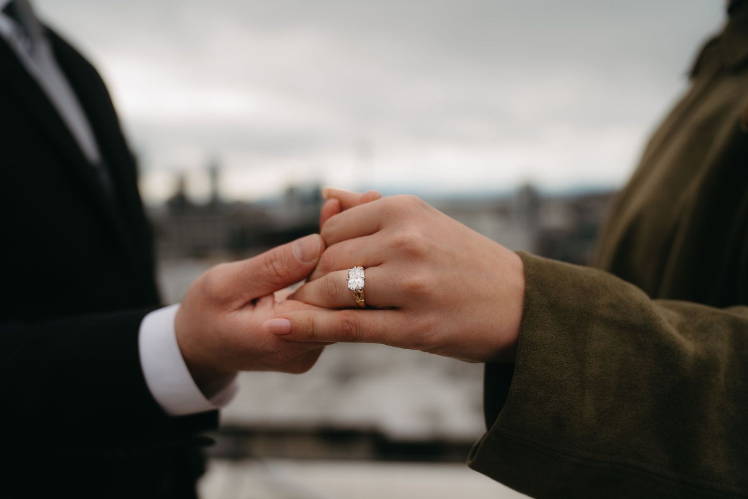 Close-up of hands with a diamond engagement ring on a cloudy day.