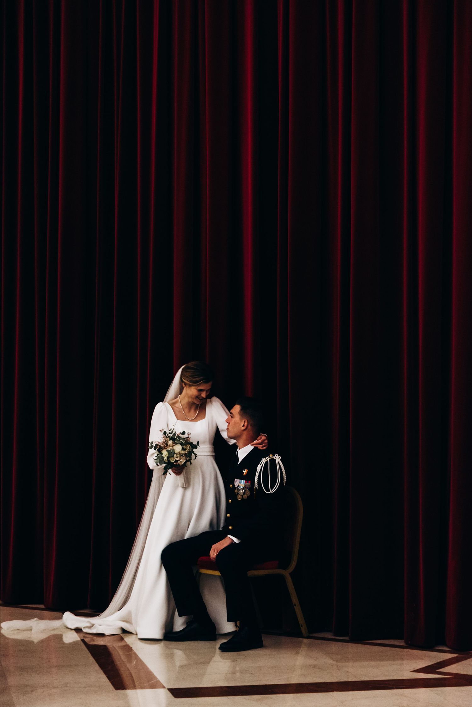 Minimalist wedding photos with dramatic lighting show couple in white dress and dark suit against red velvet curtains.