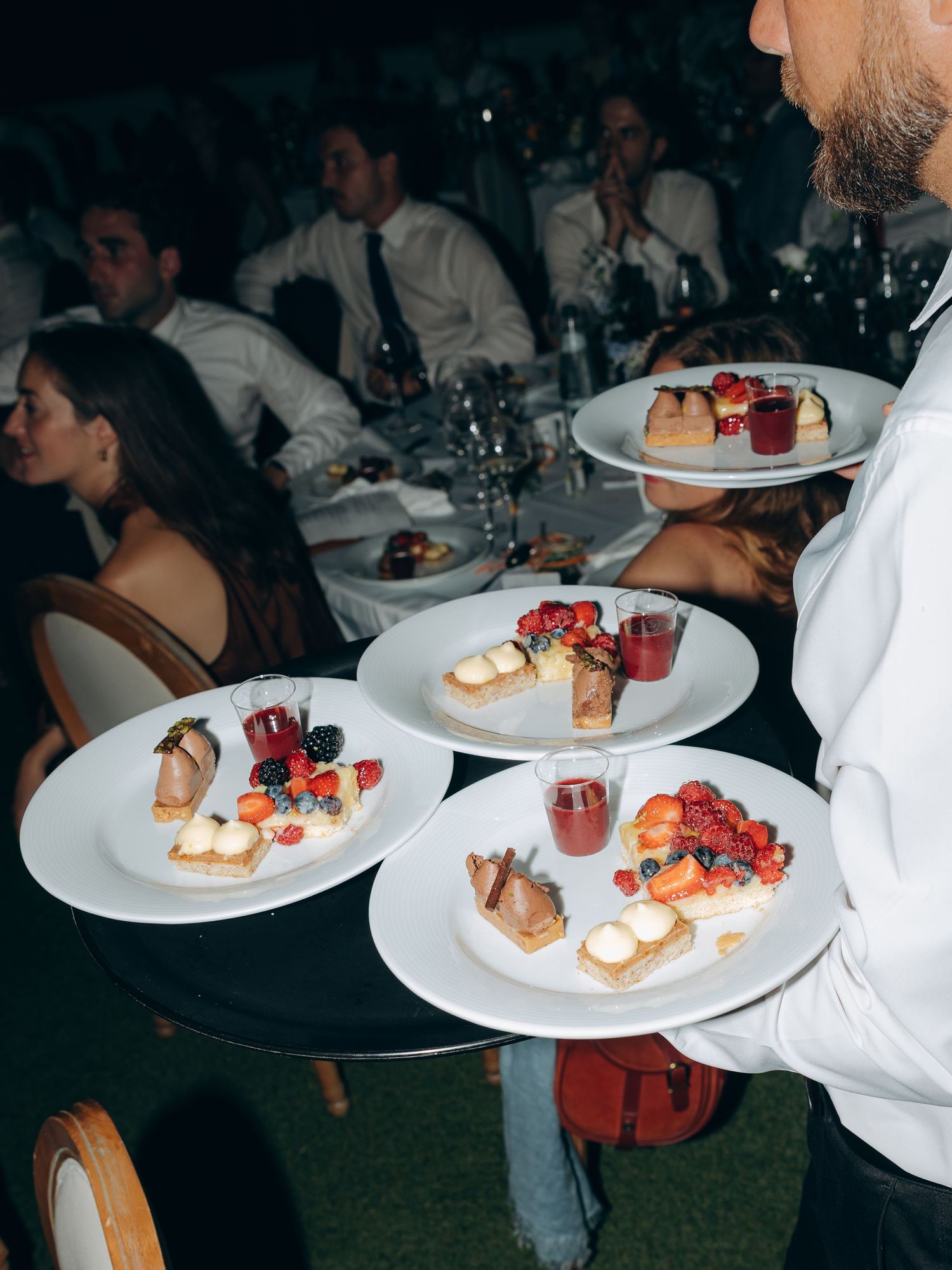 Waiter serving elegant dessert plates with fresh berries and pastries to guests at a formal dinner event.