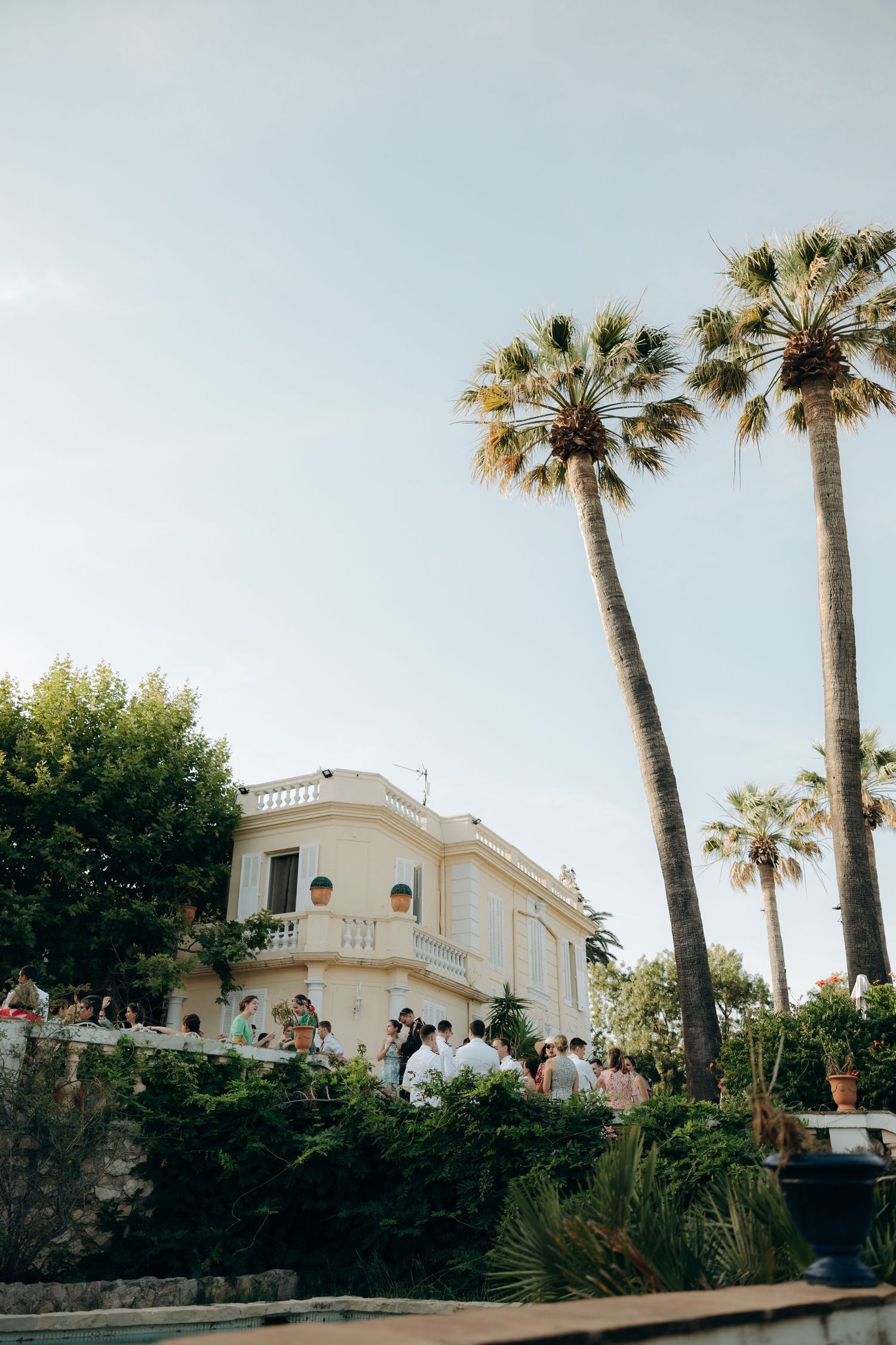 A white Mediterranean villa with tall palm trees against a light blue sky.