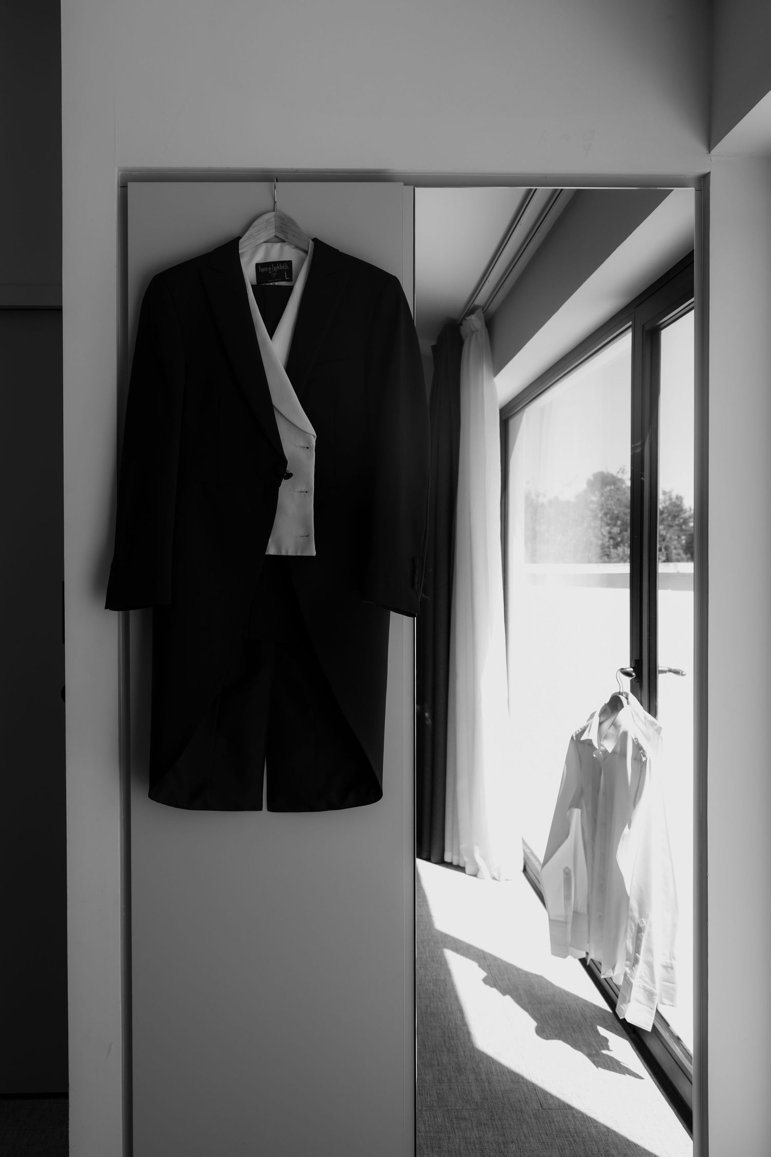 Black and white formal attire hanging in a sunlit dressing room.