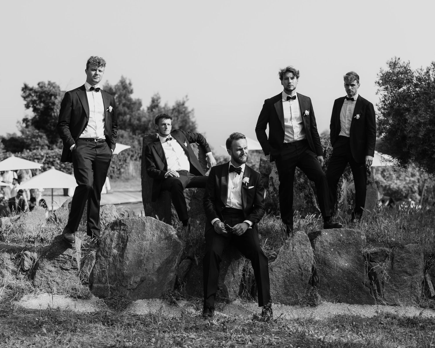 Black and white portrait of formally dressed group posing on rocky terrain.