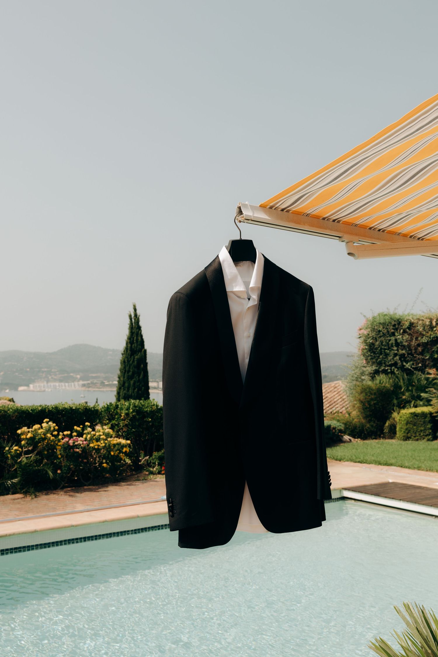 A black formal suit jacket hanging outdoors with a swimming pool and mountain landscape in the background.