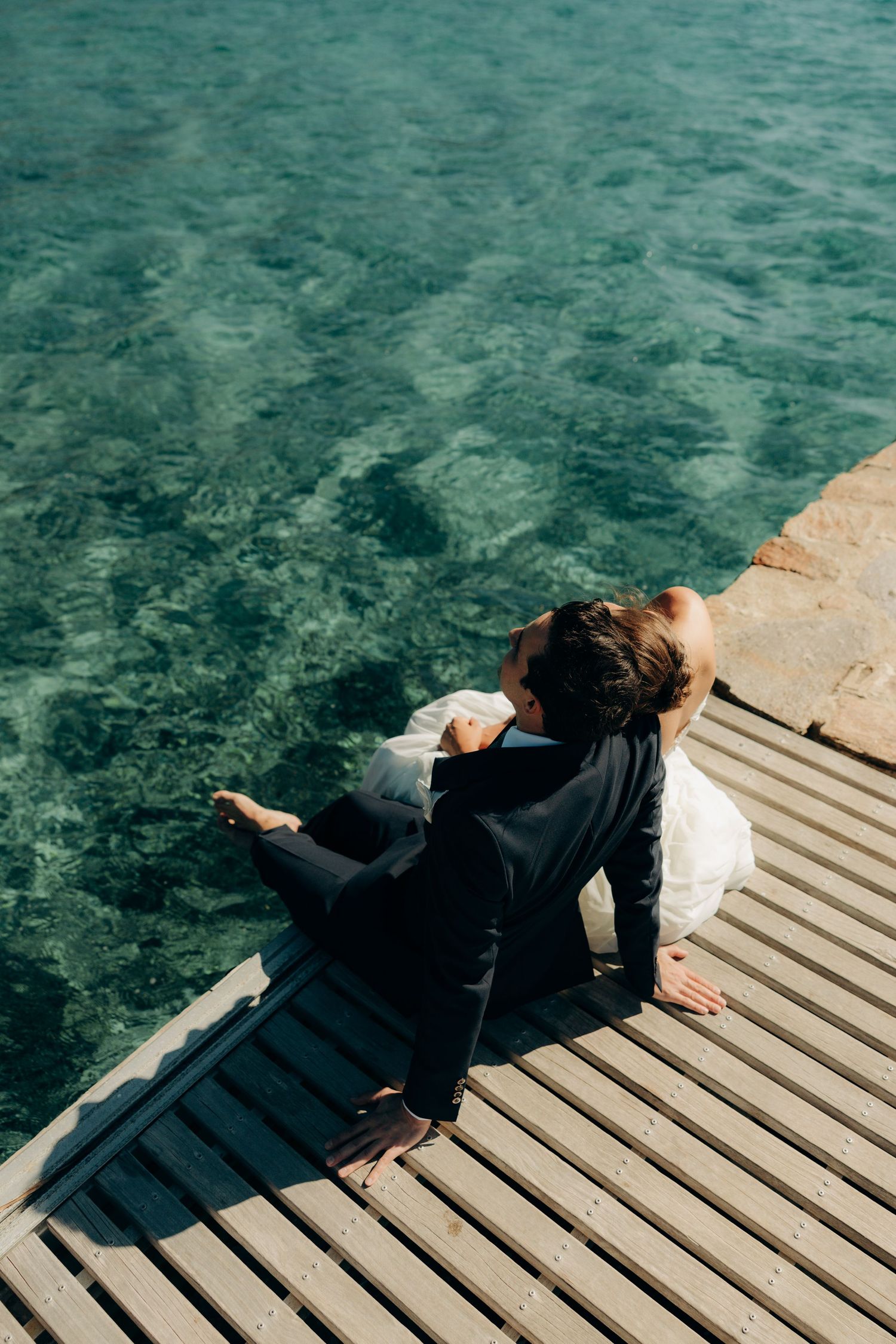 A sequence of artistic shots showing a person lying on a wooden dock over crystal clear turquoise waters.