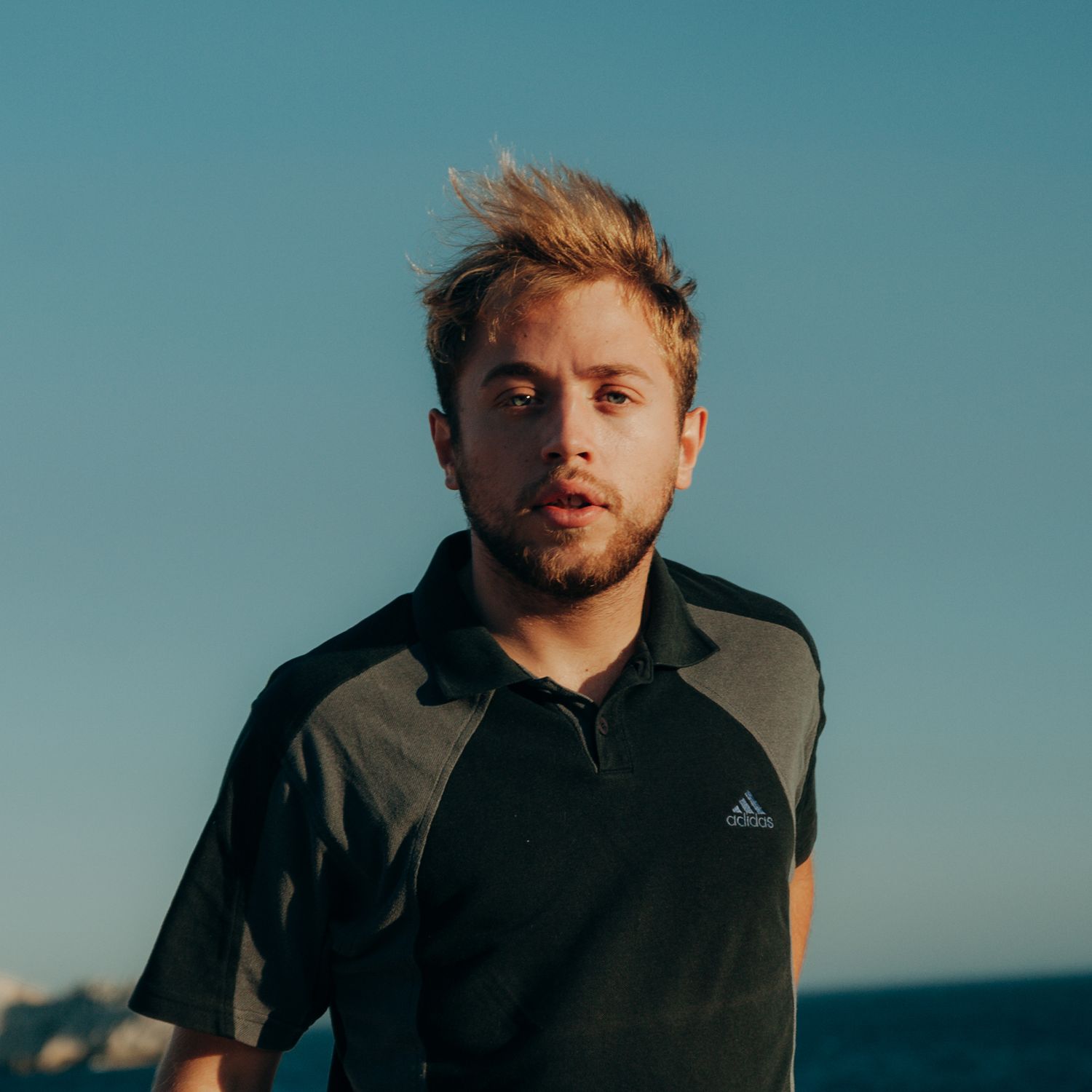 Athletic figure in black activewear stands against blue sky background in moody sunset lighting.
